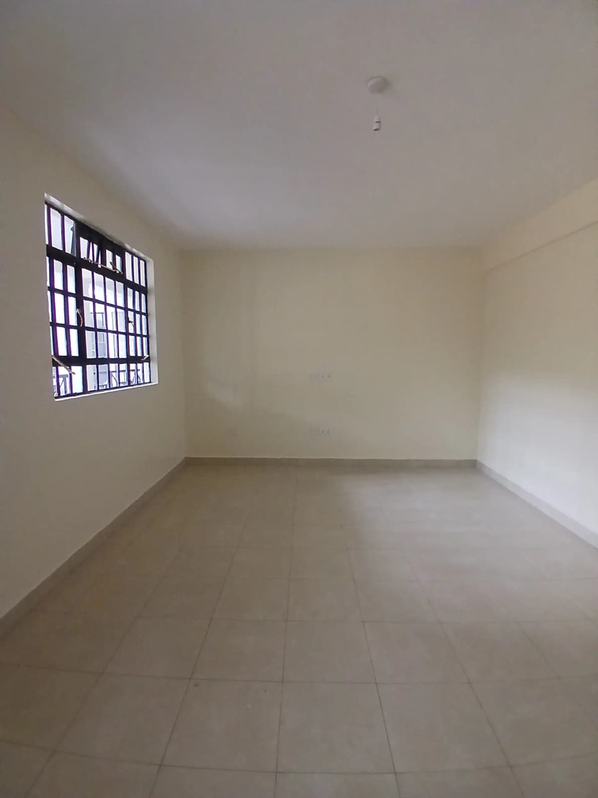 Empty bedroom with barred window and tiled flooring
