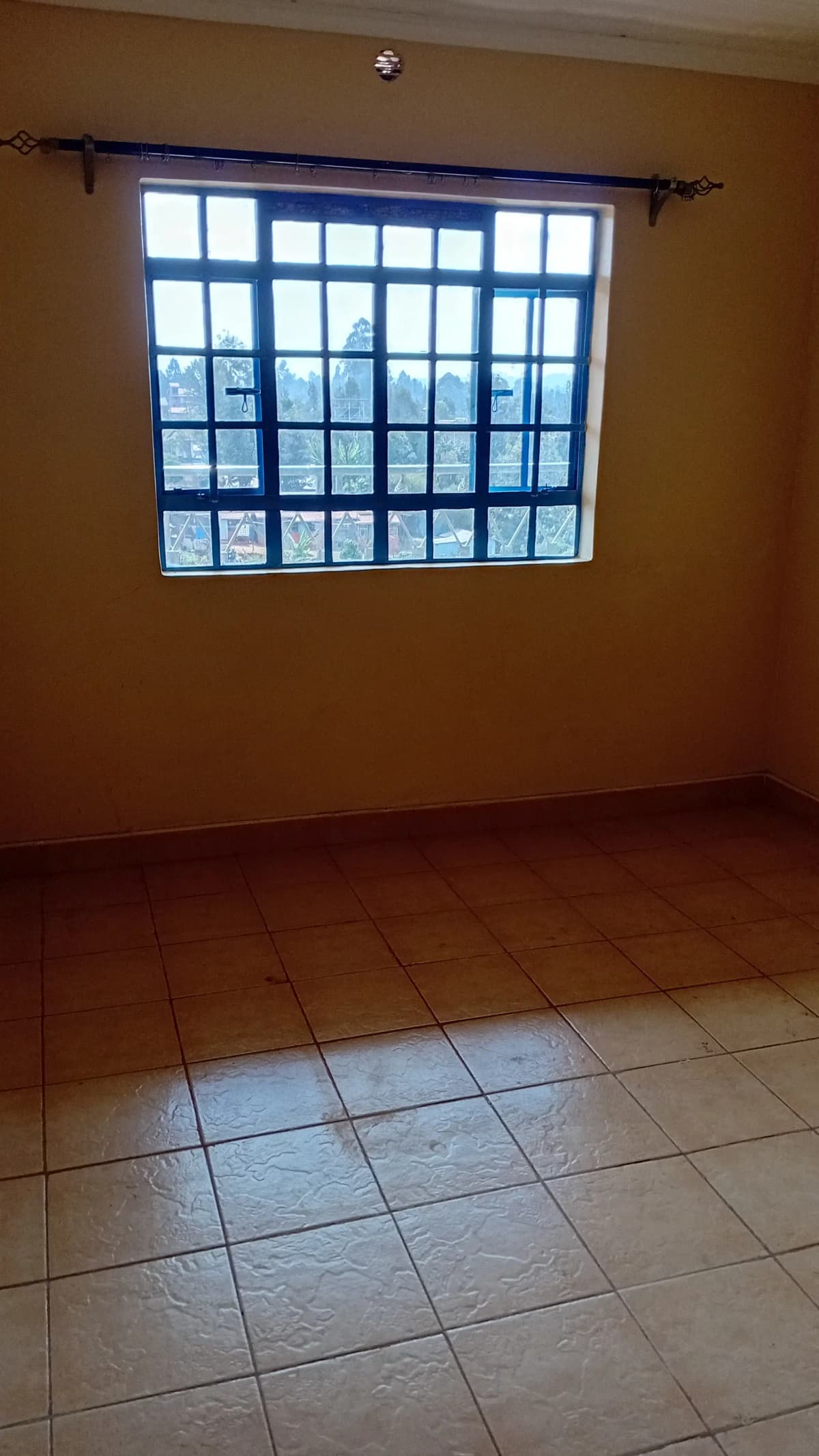 Empty bedroom with large barred window and terracotta tile flooring