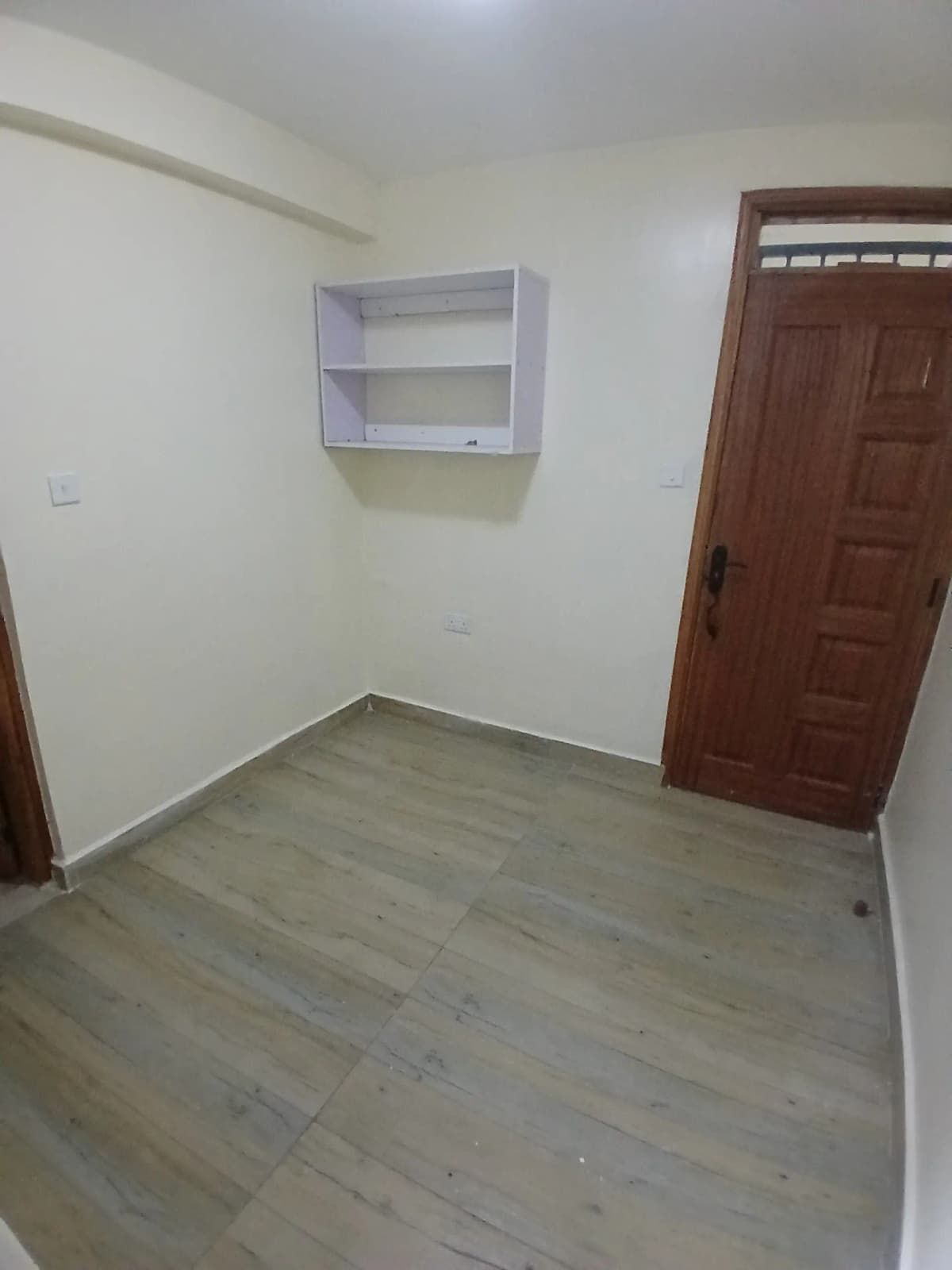 Sparse bedroom with wall-mounted shelving and wooden door
