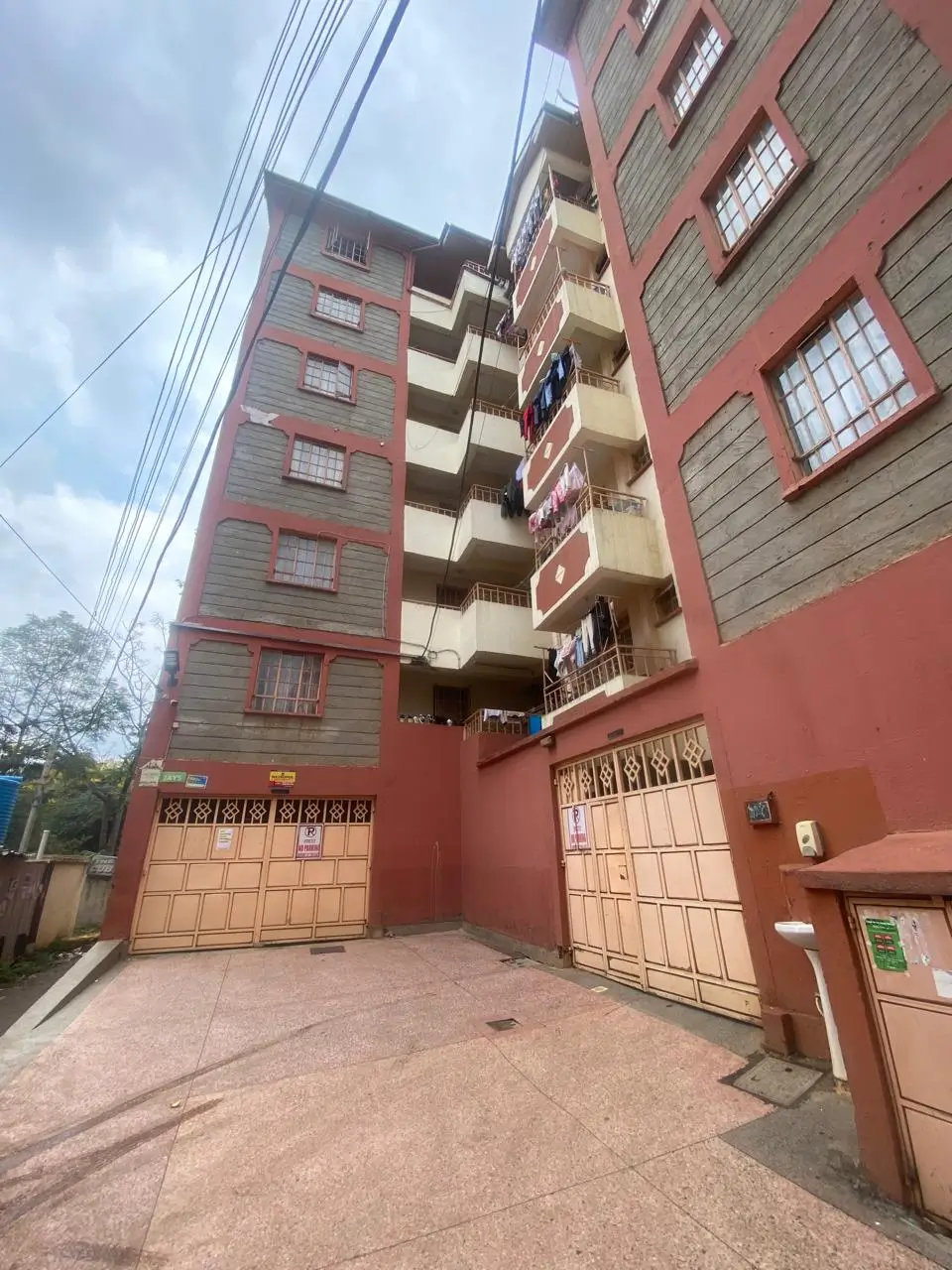 Multi-story residential building with red facade and parking gates