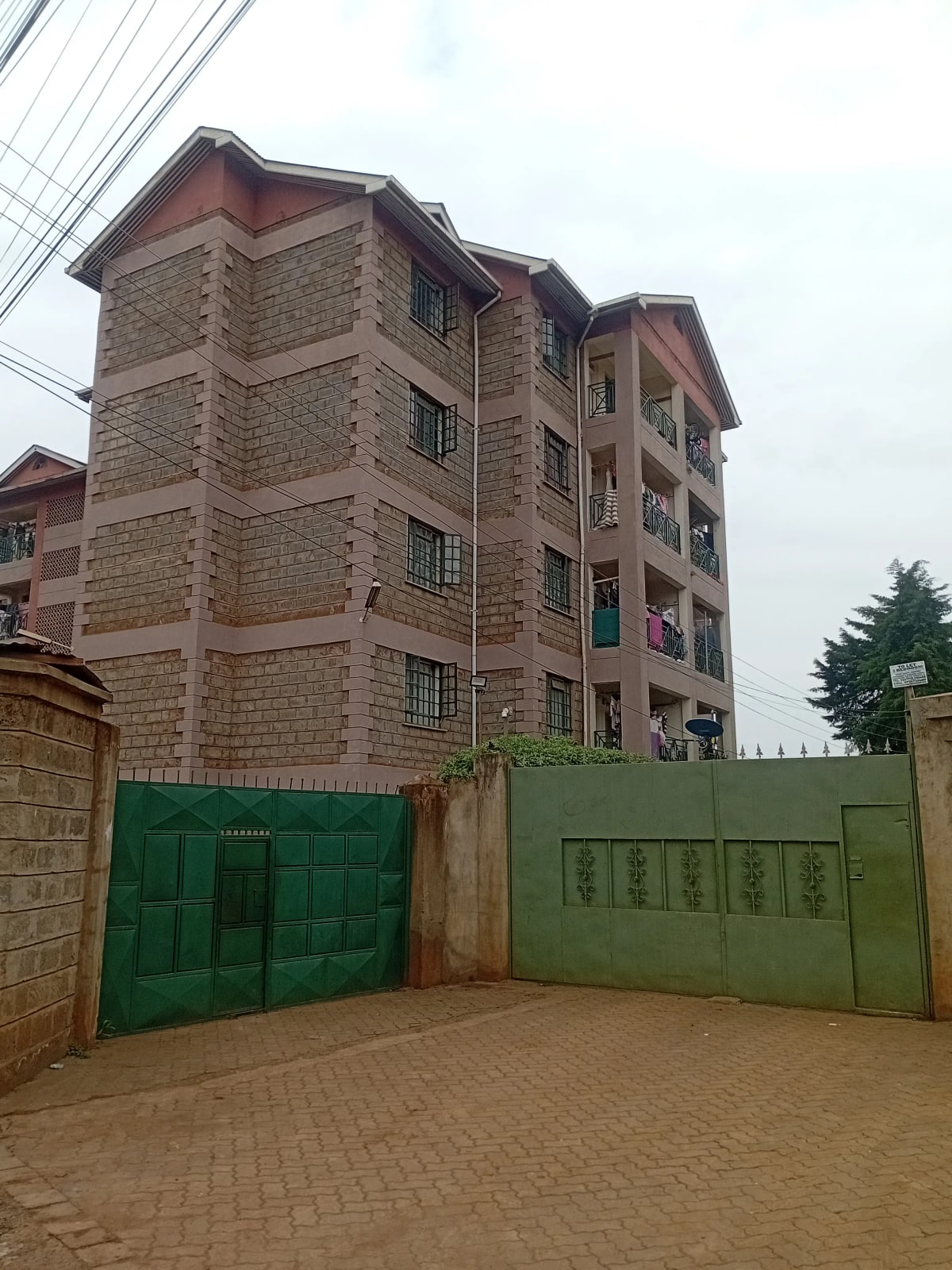 Multi-story residential building with green compound gates and driveway