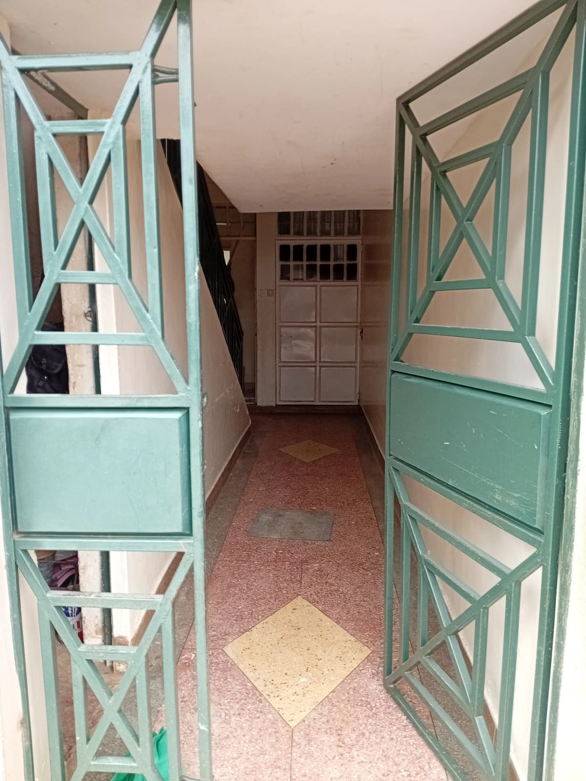 Narrow hallway with turquoise X-pattern doors and red tile flooring