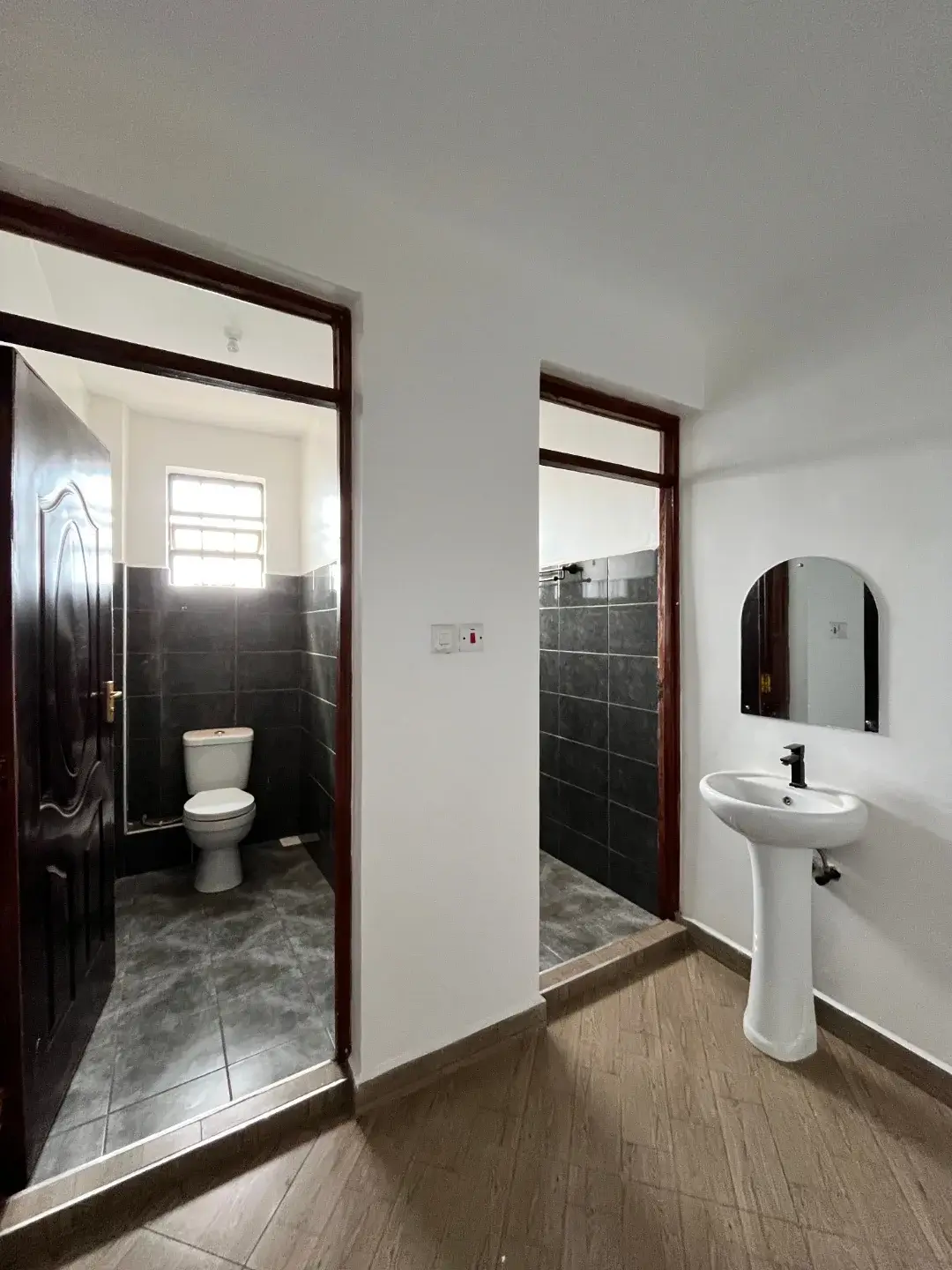 Modern bathroom with black tile, pedestal sink, toilet
