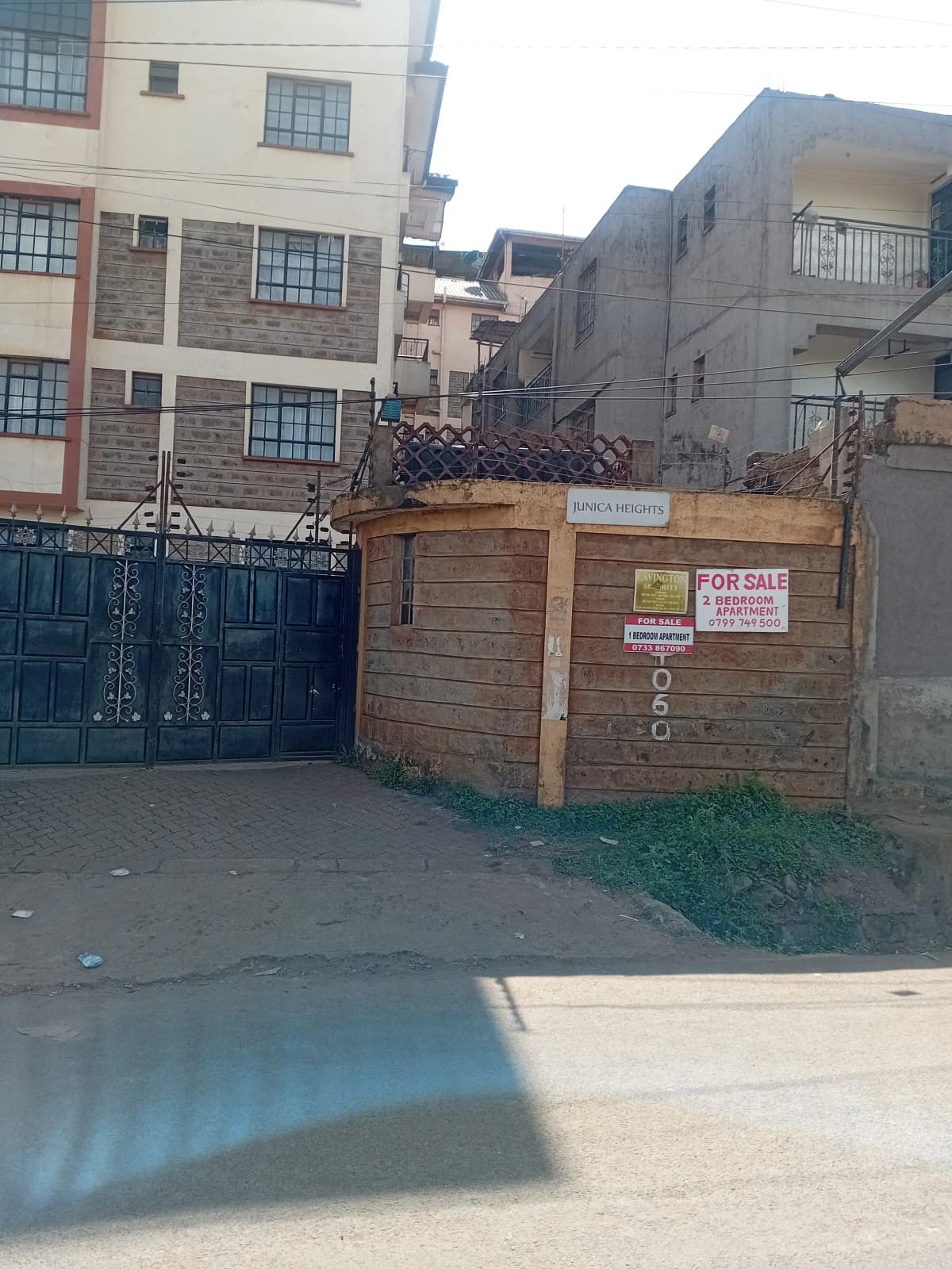 Residential compound entrance with wooden gate and FOR SALE sign
