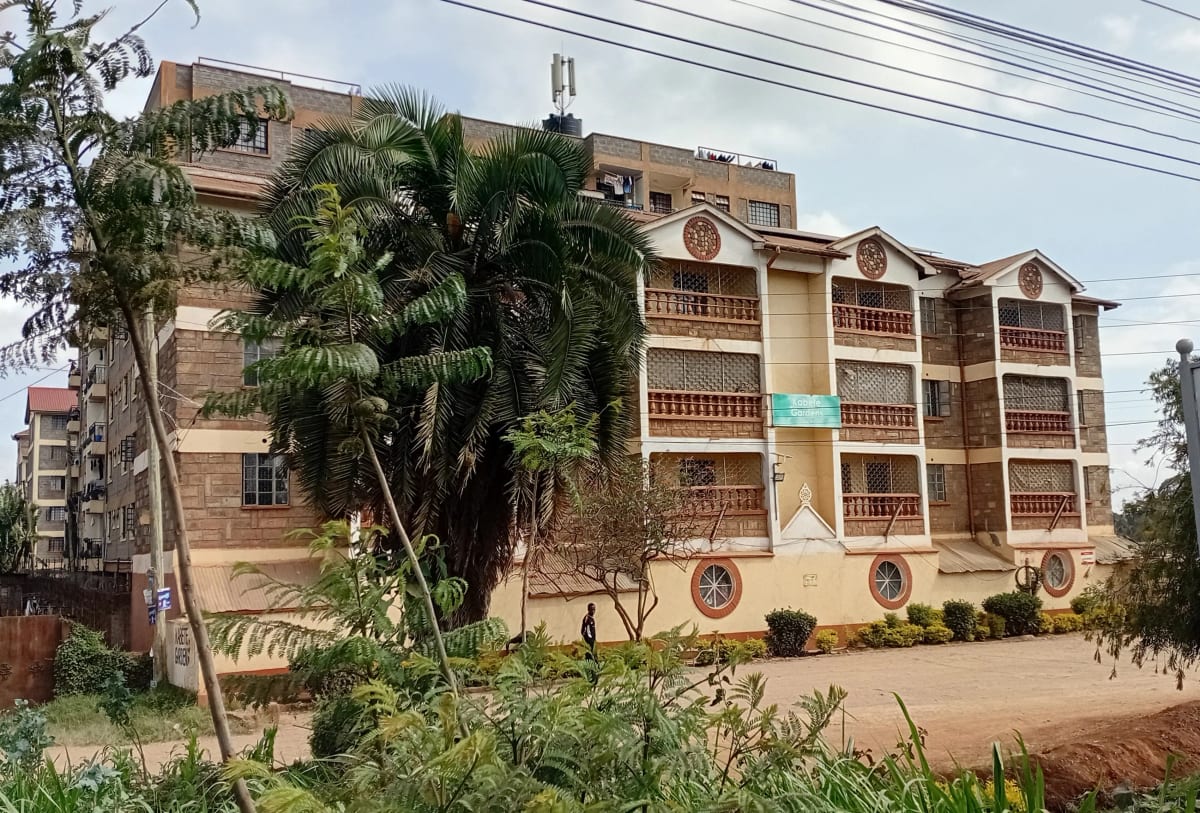 Multi-story residential building with palm trees and compound grounds