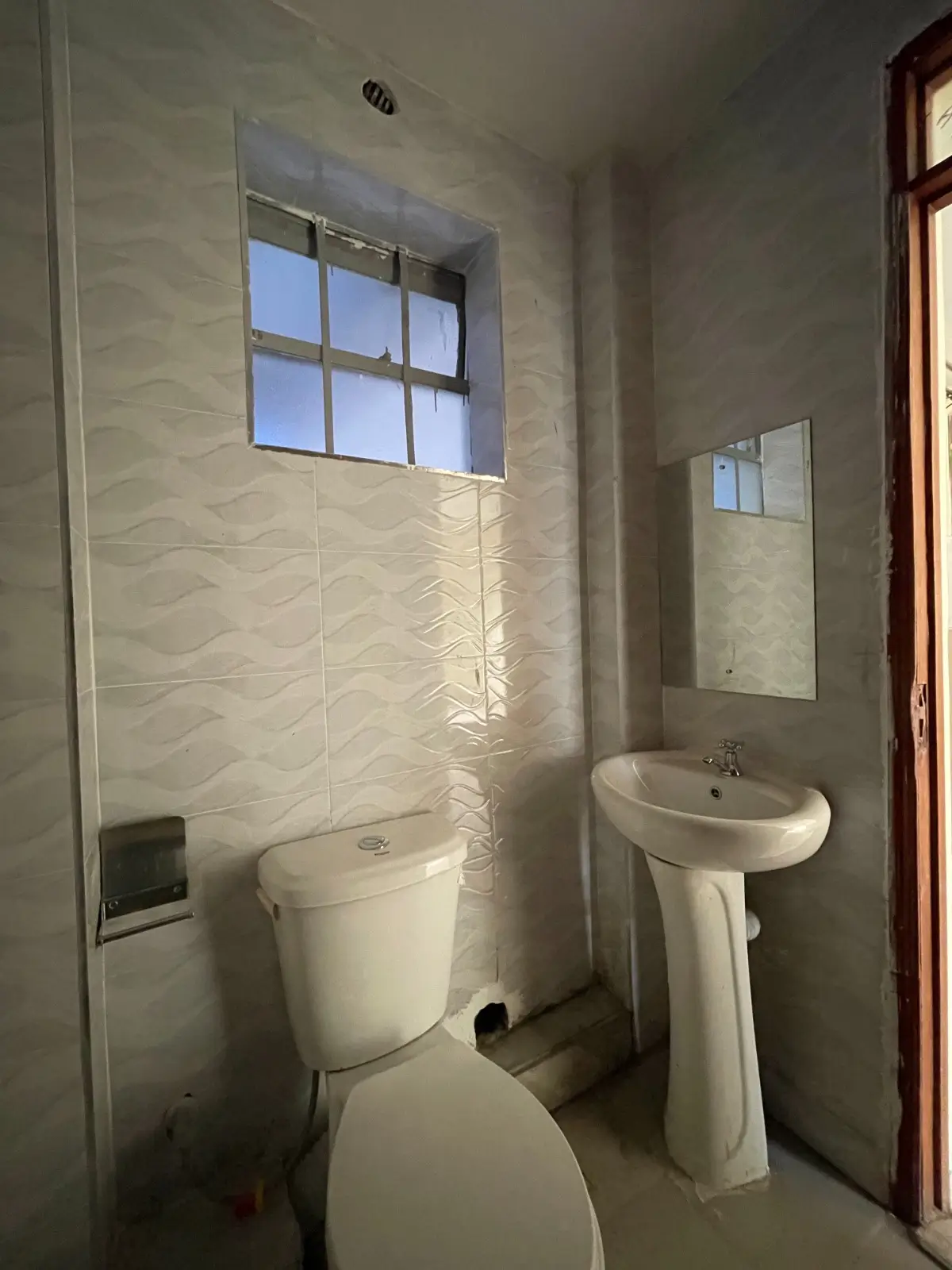 Bright bathroom with toilet, pedestal sink, tiled walls
