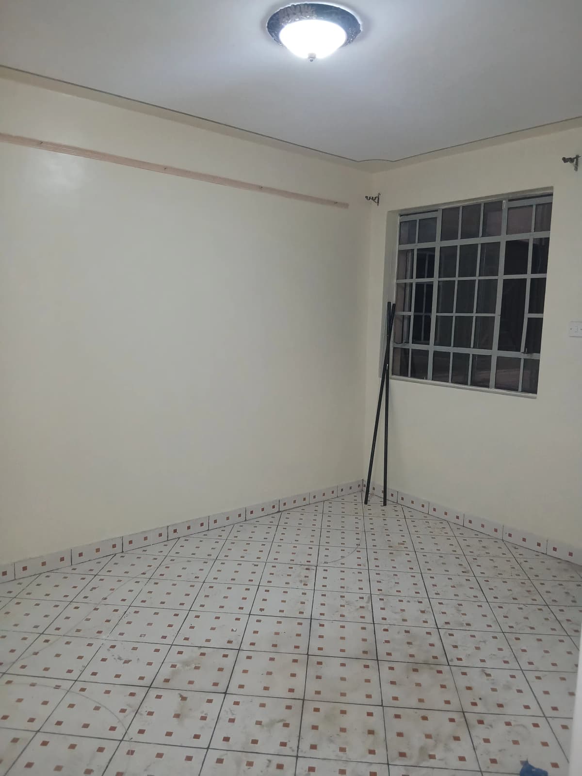 Empty bedroom with barred window and patterned tile flooring