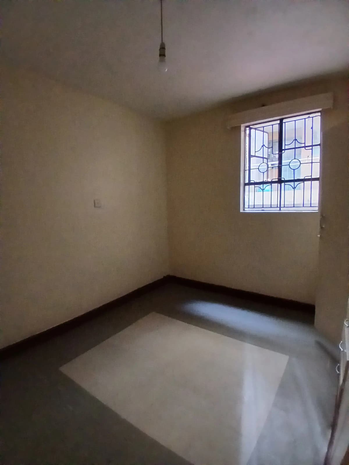 Unfurnished bedroom with barred window and concrete flooring