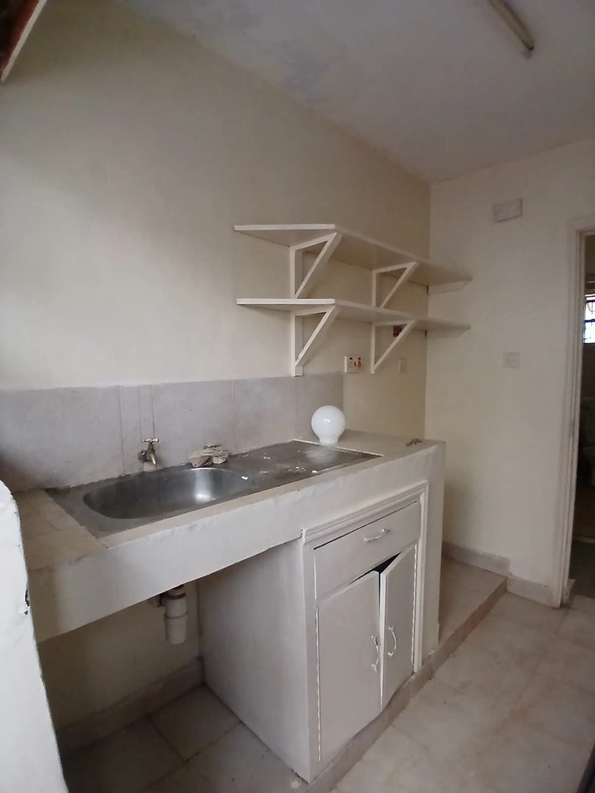 Compact kitchenette with sink, cabinet storage, open shelving