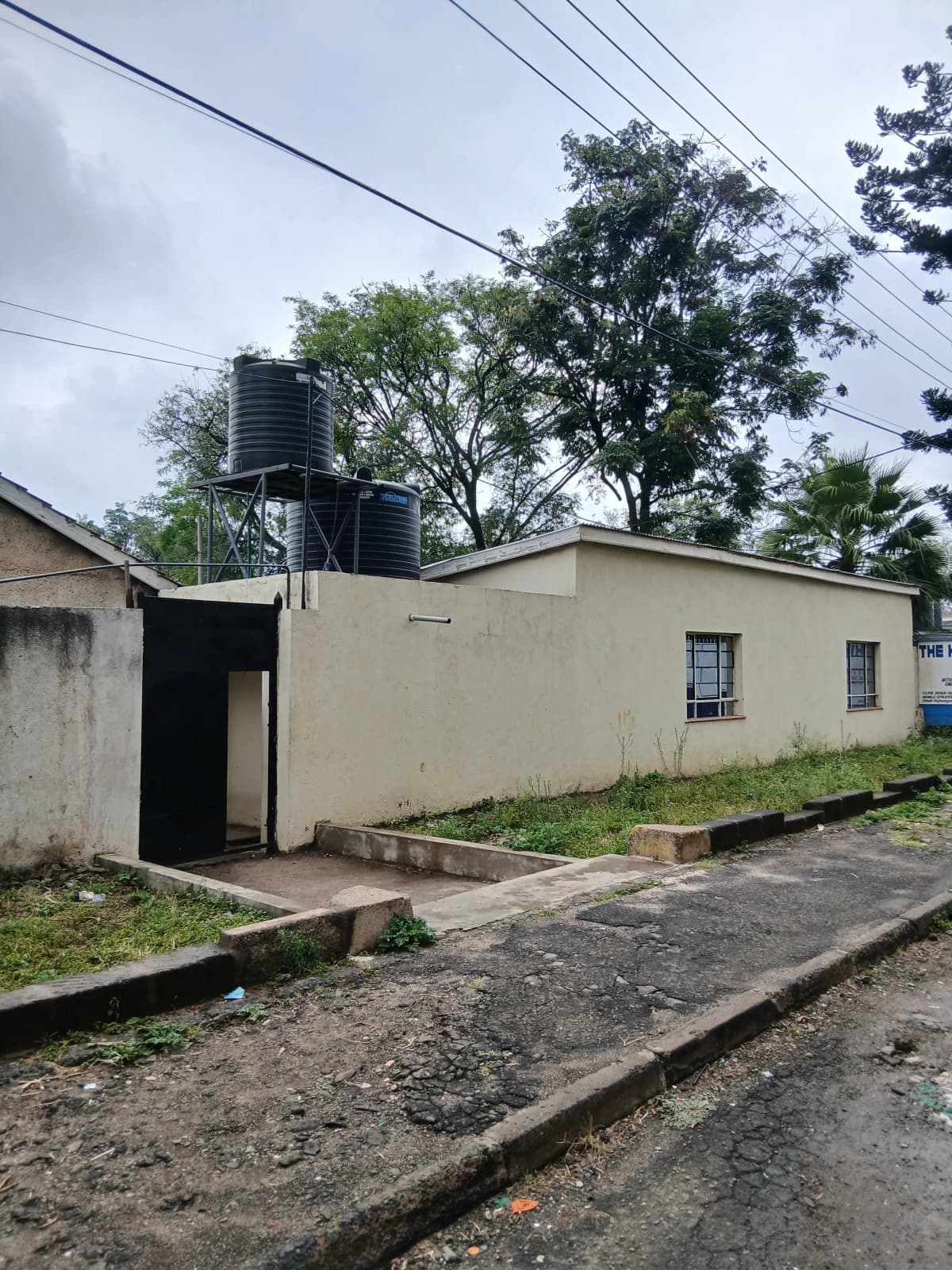 Cream-colored house facade with water tank and overgrown compound
