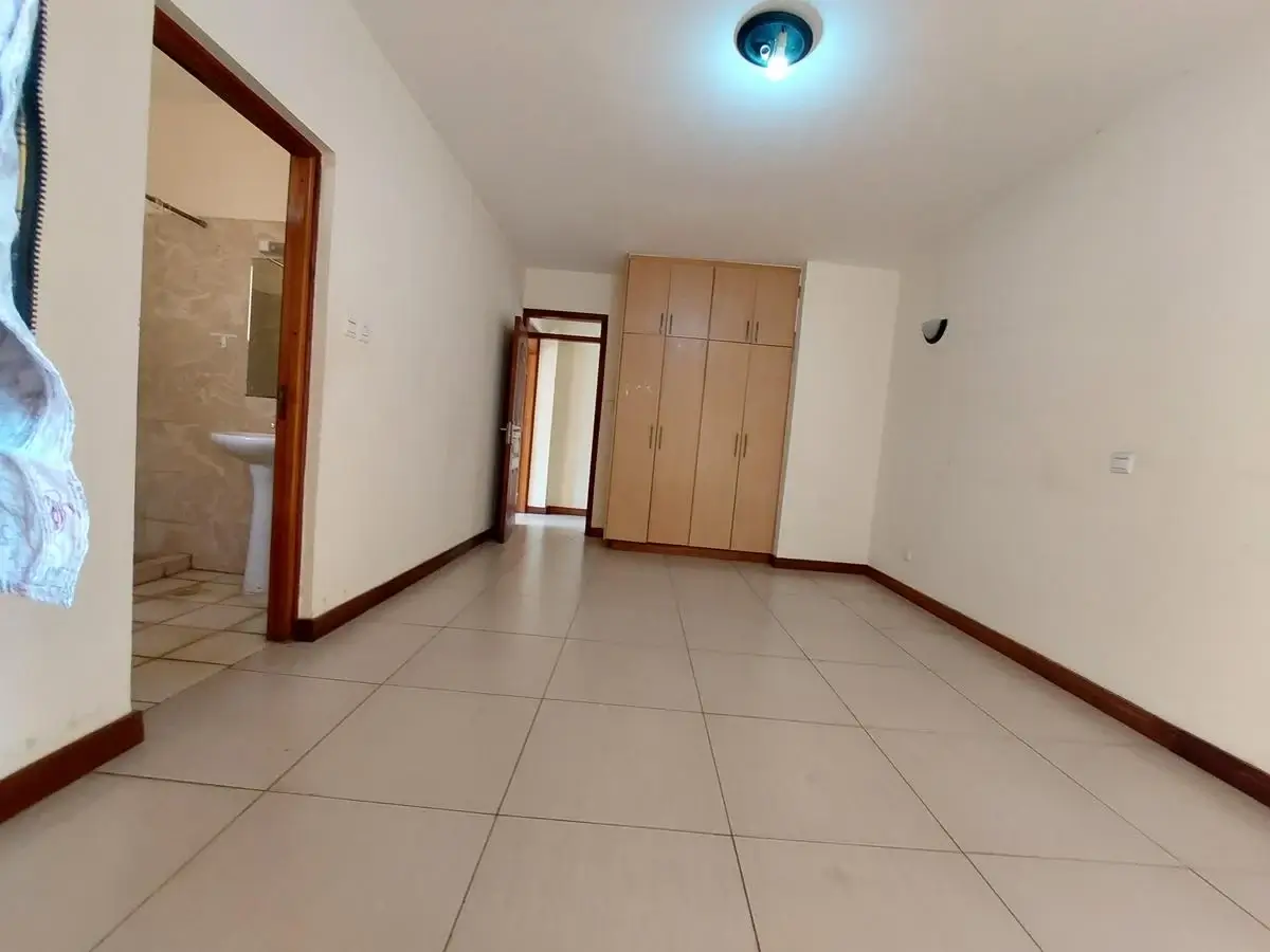 Spacious bedroom with tiled flooring and built-in wooden wardrobes