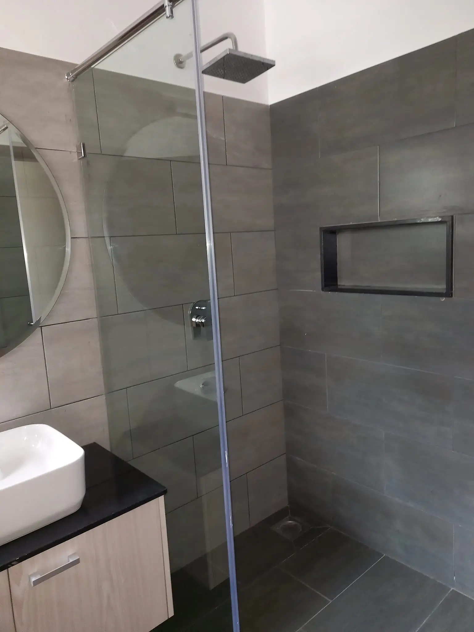 Modern bathroom with gray tile, glass shower enclosure, vanity