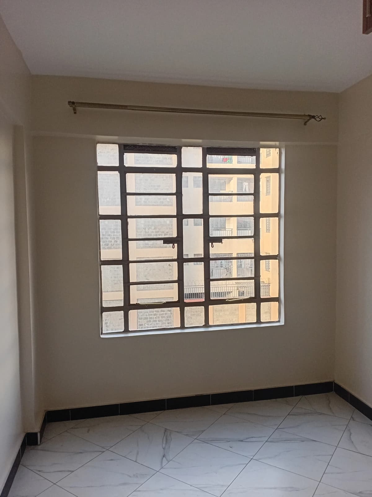 Empty bedroom with large barred window and tiled floor