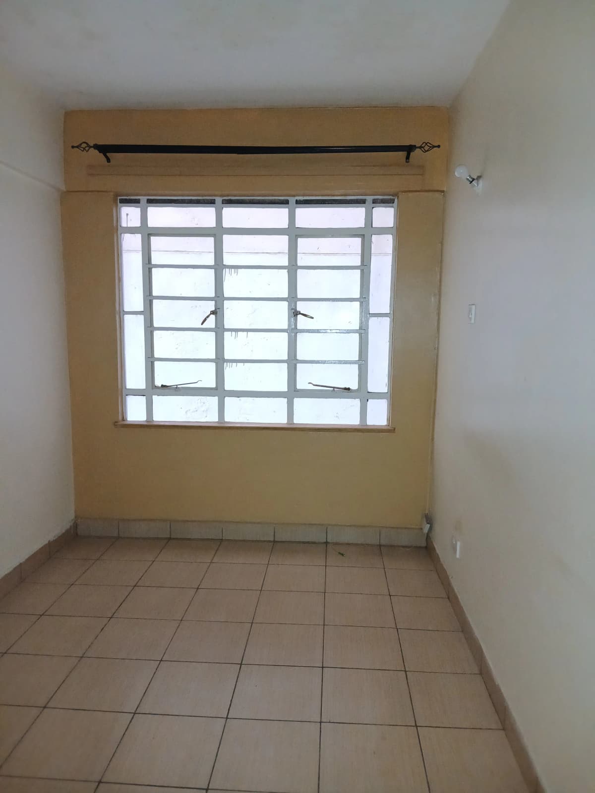 Spacious bedroom with barred window and tiled flooring