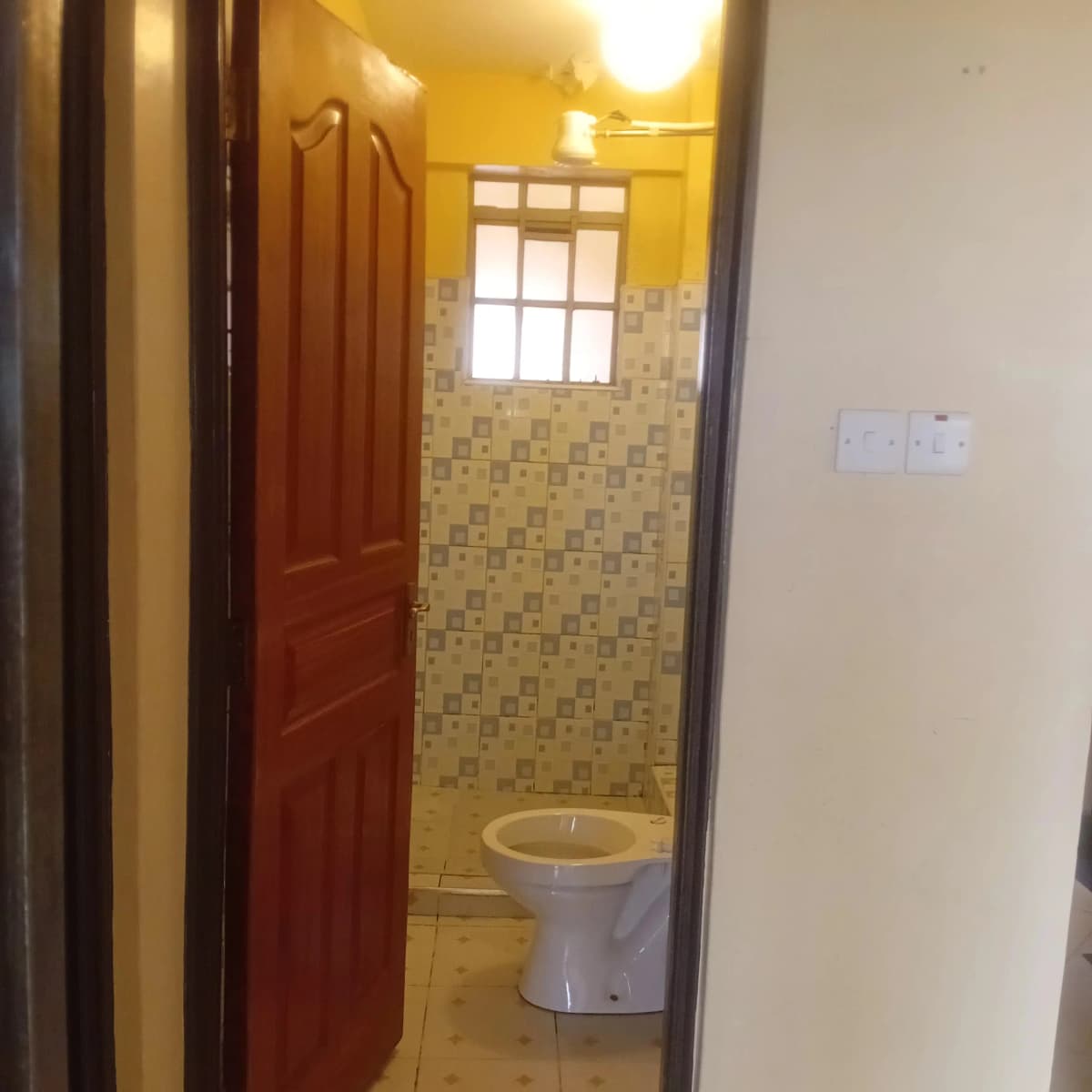 Simple bathroom with toilet, yellow tile walls, small window