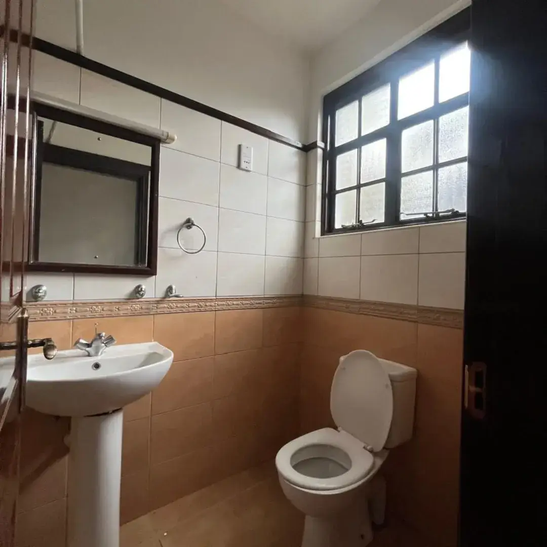 Spacious bathroom with pedestal sink, toilet, and large window