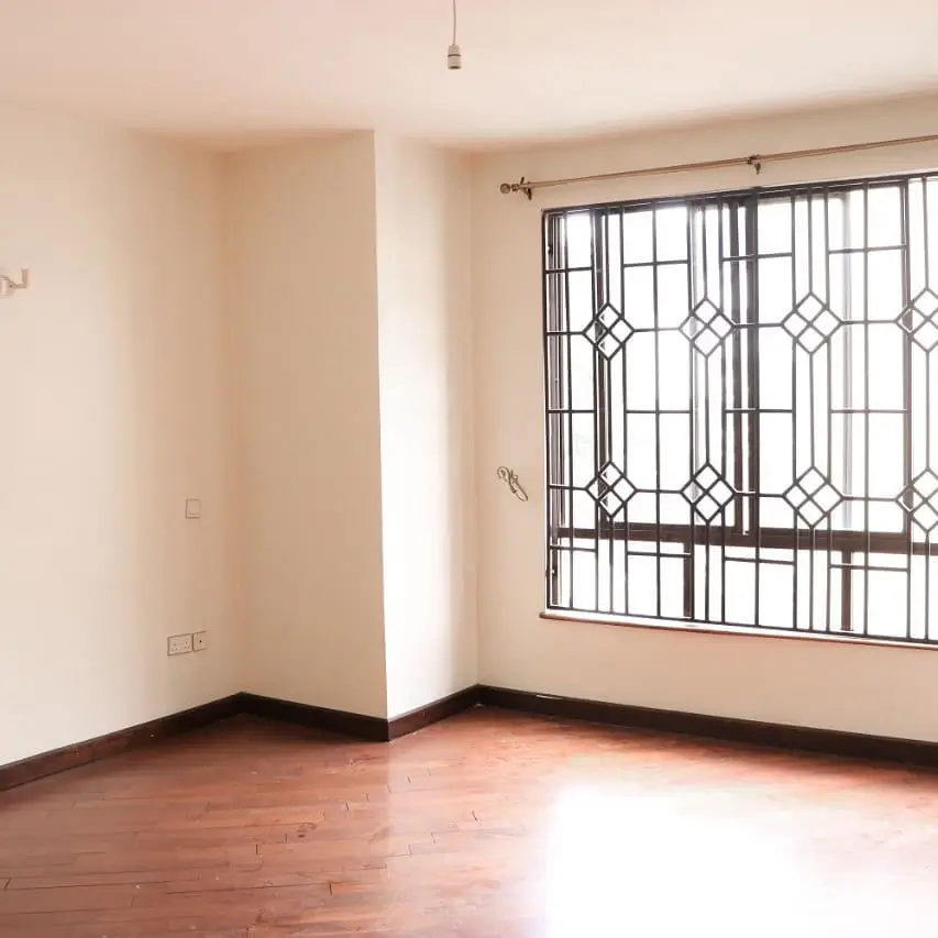 Spacious bedroom with wooden flooring and barred window