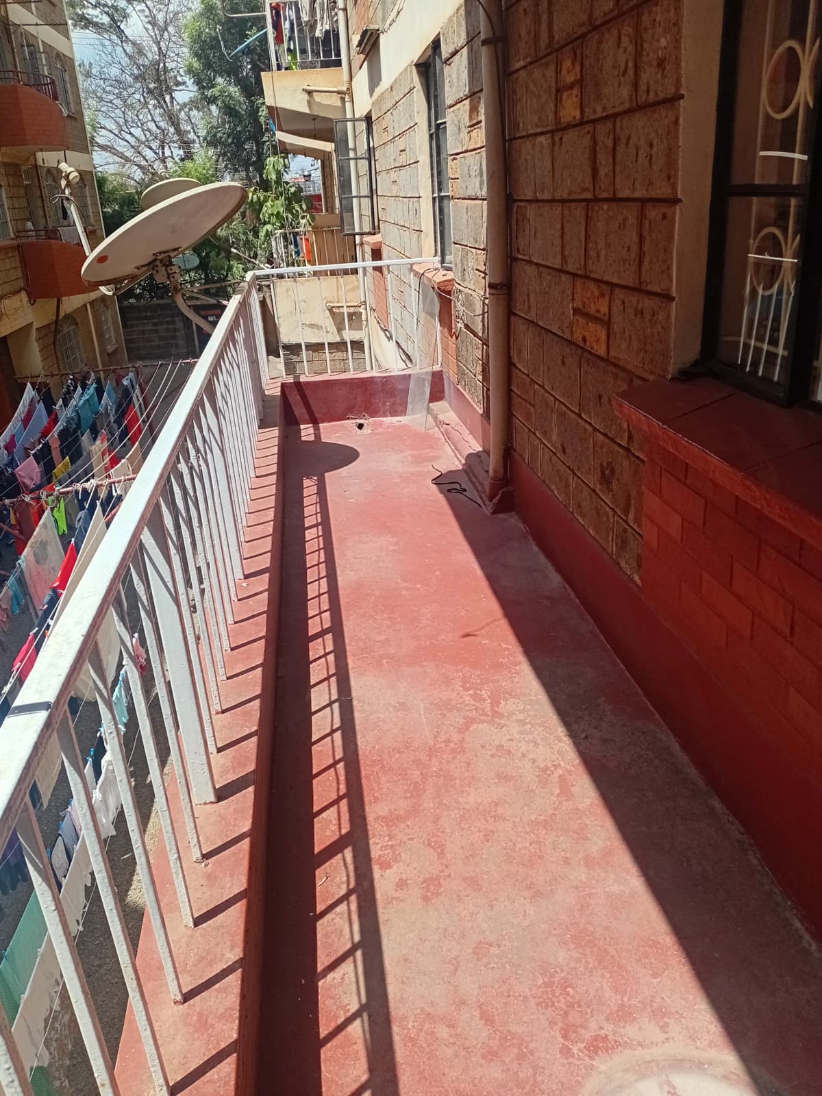 Narrow red-tiled balcony with white railing and clothesline