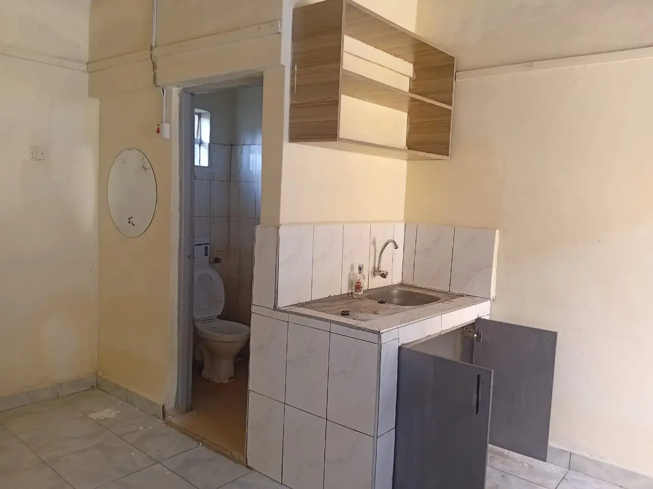 Compact kitchen with white cabinetry and sink; bathroom visible through doorway