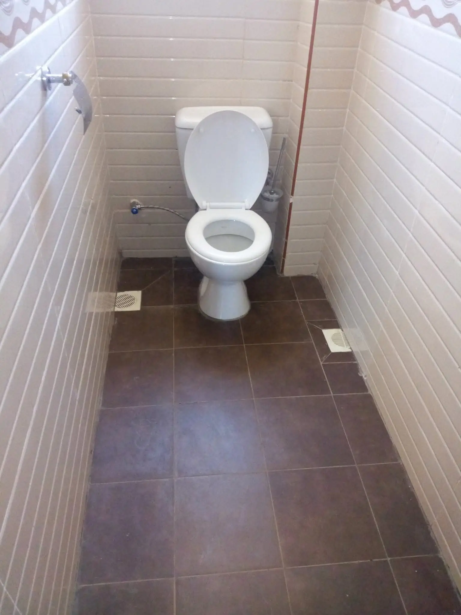 Compact toilet room with white ceramic fixture and dark tile flooring