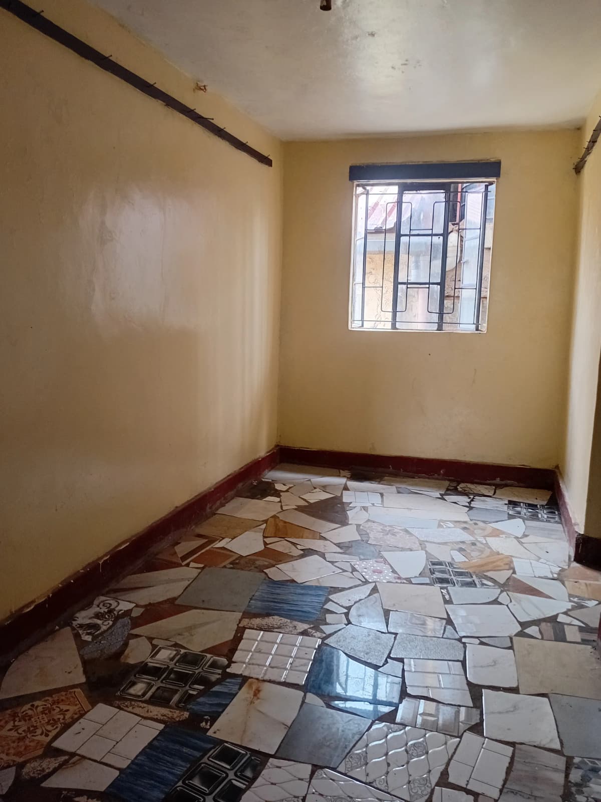 Unfurnished bedroom with barred window and tiled flooring