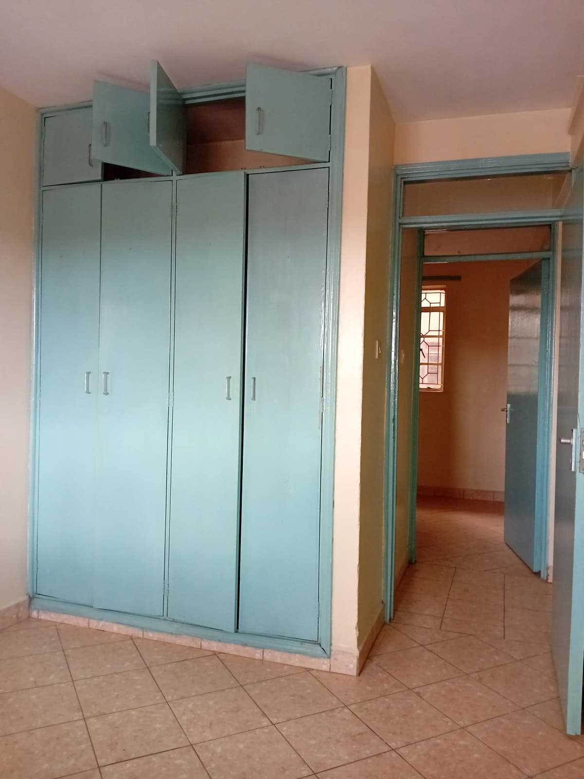 Bedroom with built-in turquoise wardrobes and terracotta flooring