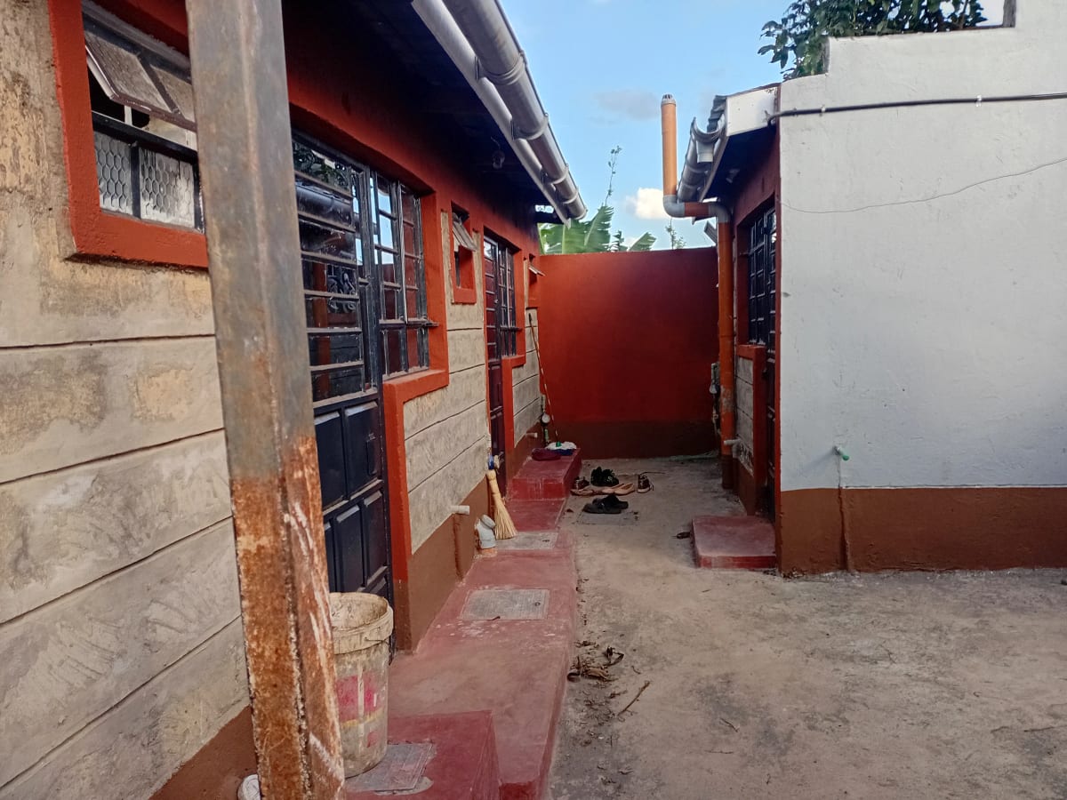 Compound entrance with red gate and single-story residential building