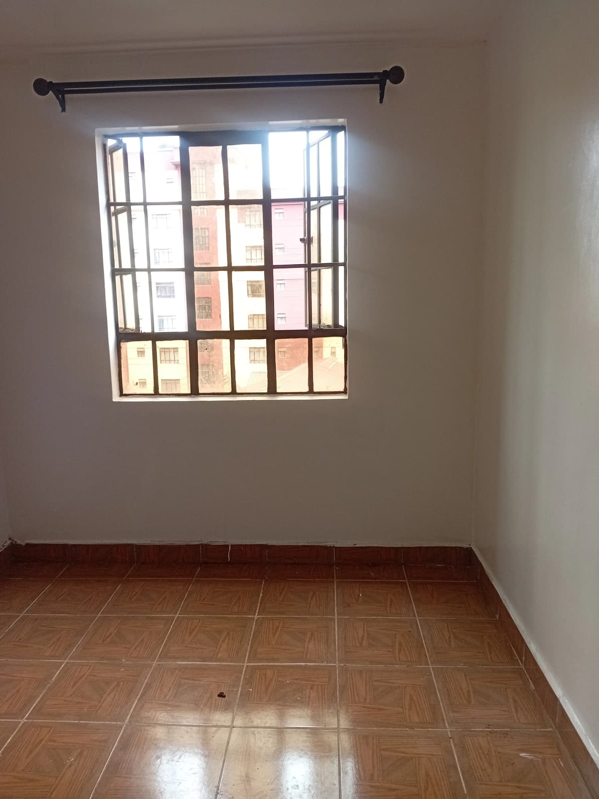 Unfurnished bedroom with barred window and terracotta tile floor