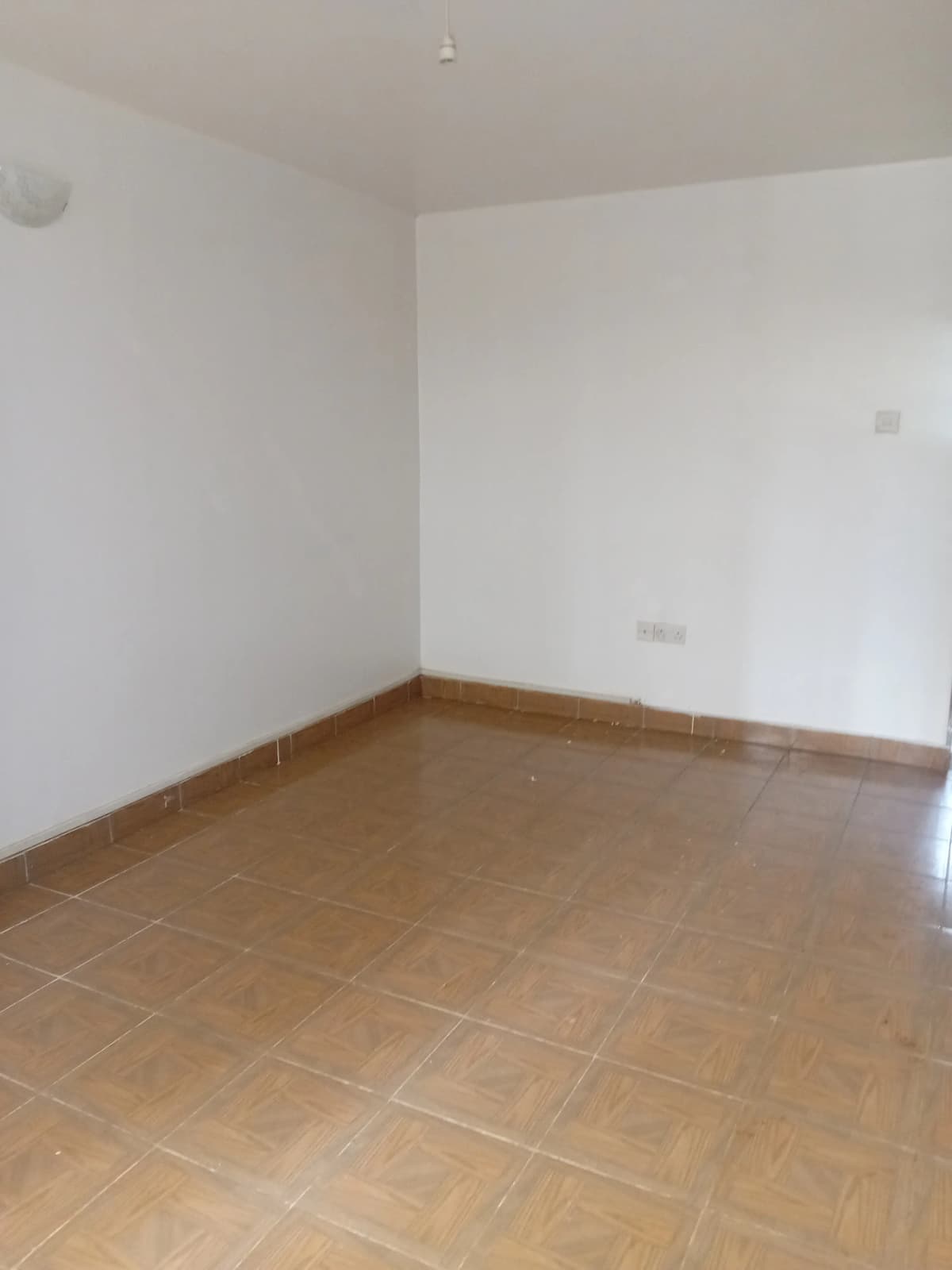 Empty living room with terracotta tile flooring and white walls