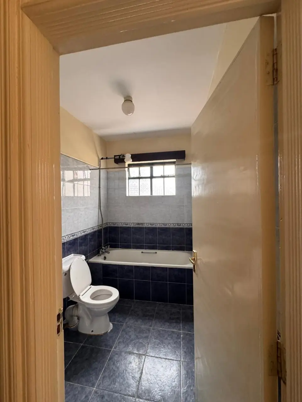Dark-tiled bathroom with bathtub, toilet, and window.