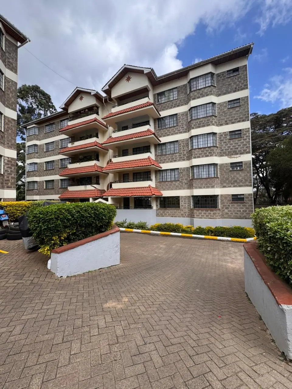 Multi-story residential building with red-trimmed balconies, landscaped compound