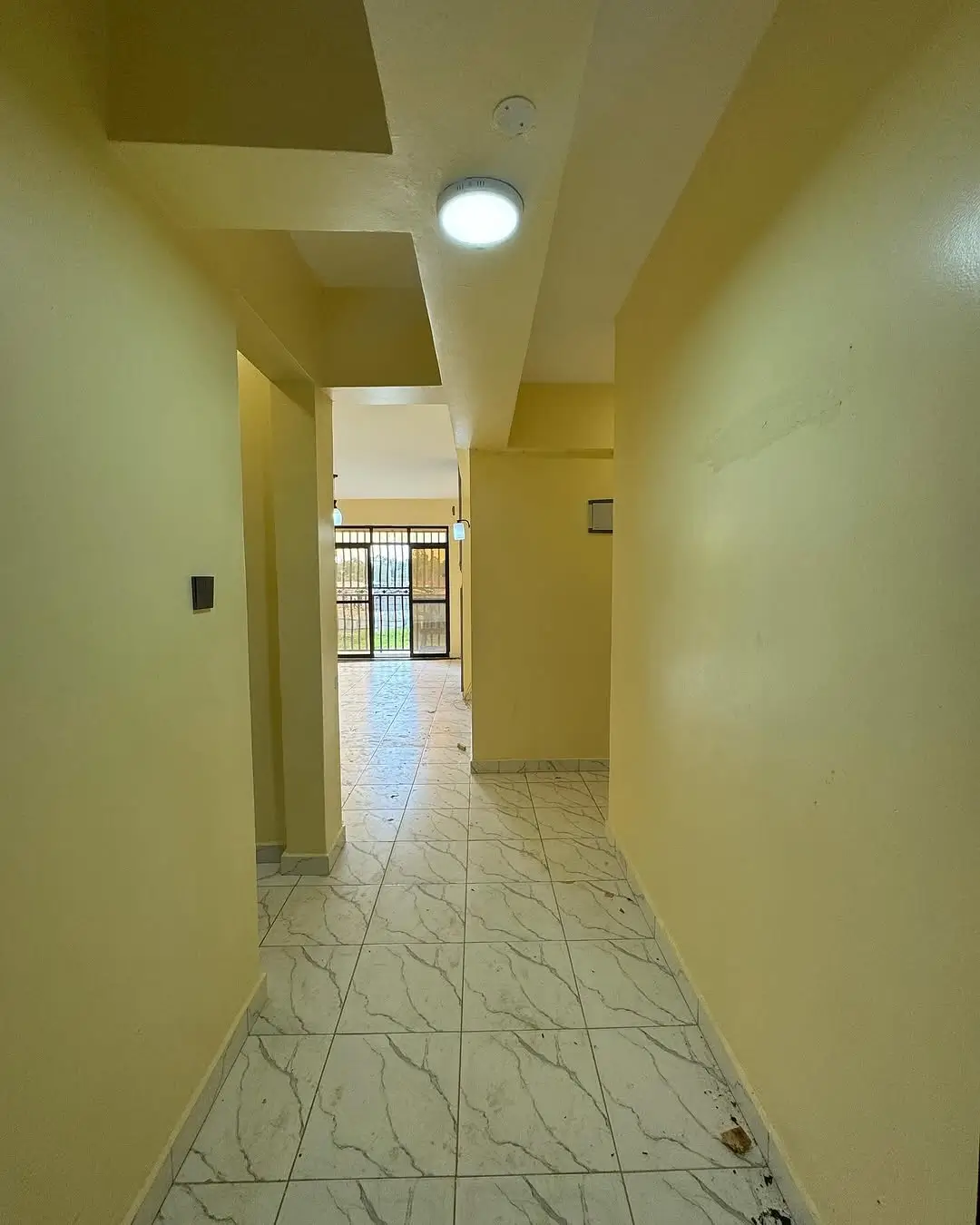 Narrow hallway with marble flooring and yellow walls