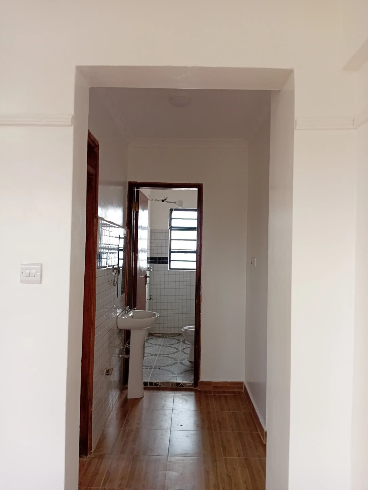 Narrow hallway with wooden flooring leading to bathroom