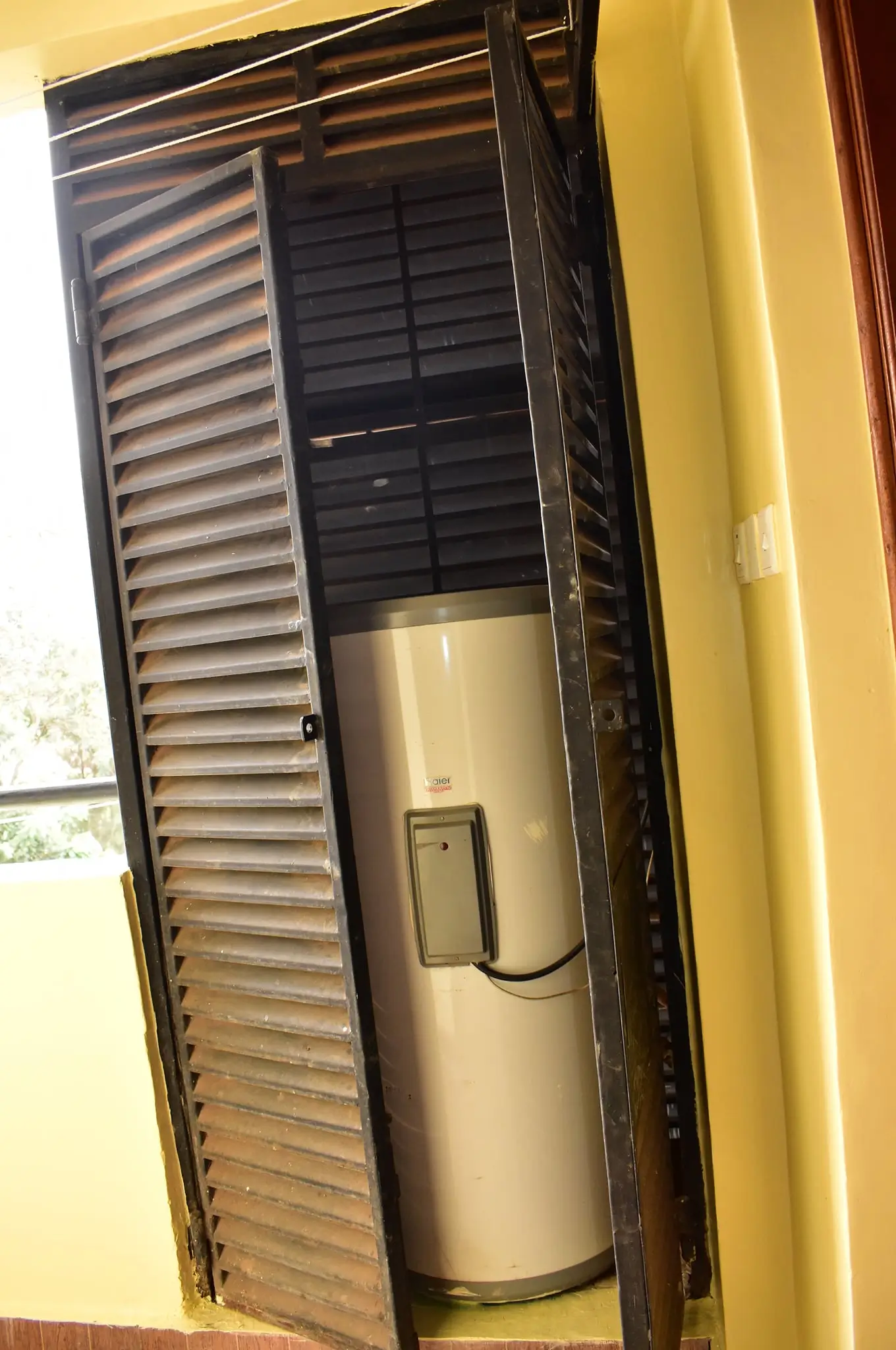 Water heater unit in wall-mounted enclosure with louvered doors
