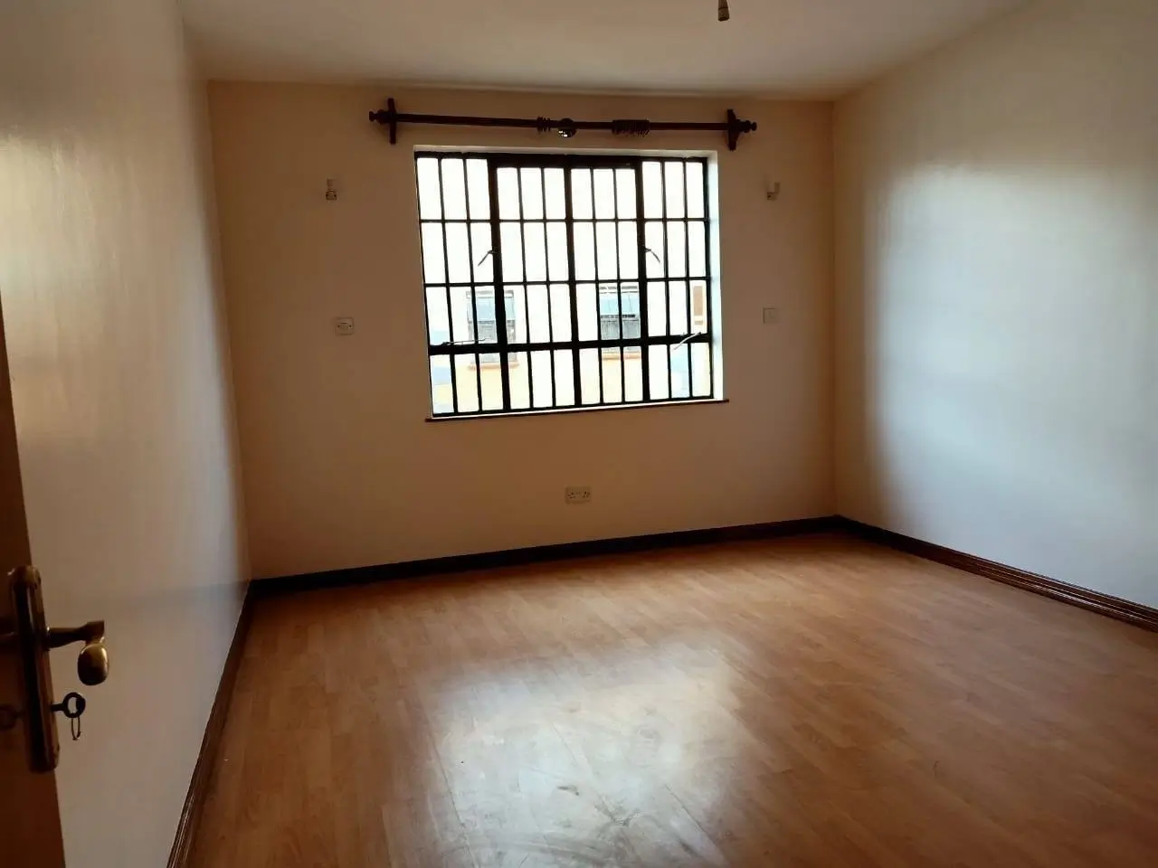 Spacious bedroom with wooden floors and barred window