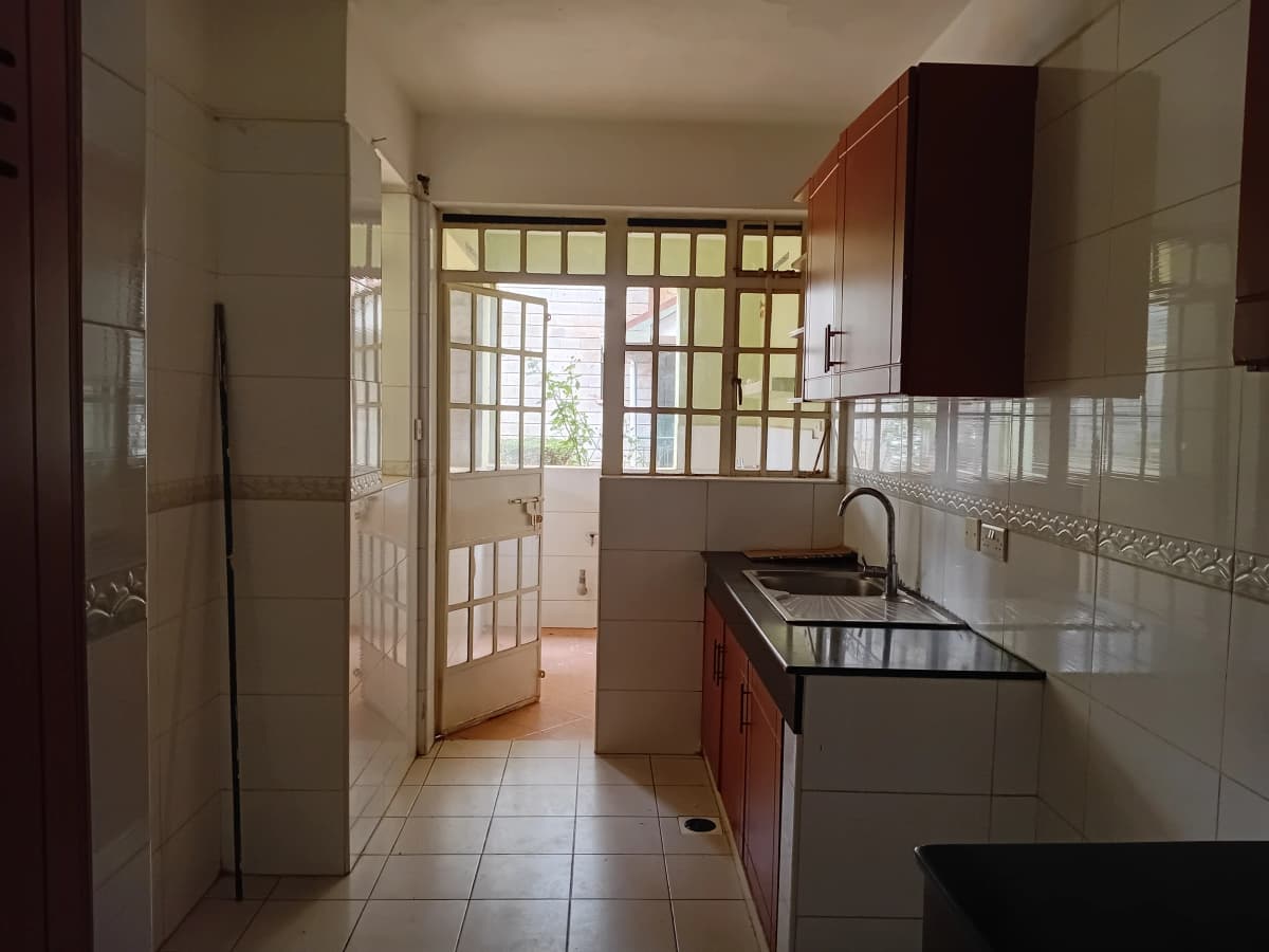 Galley kitchen with red cabinets, sink, and garden view beyond
