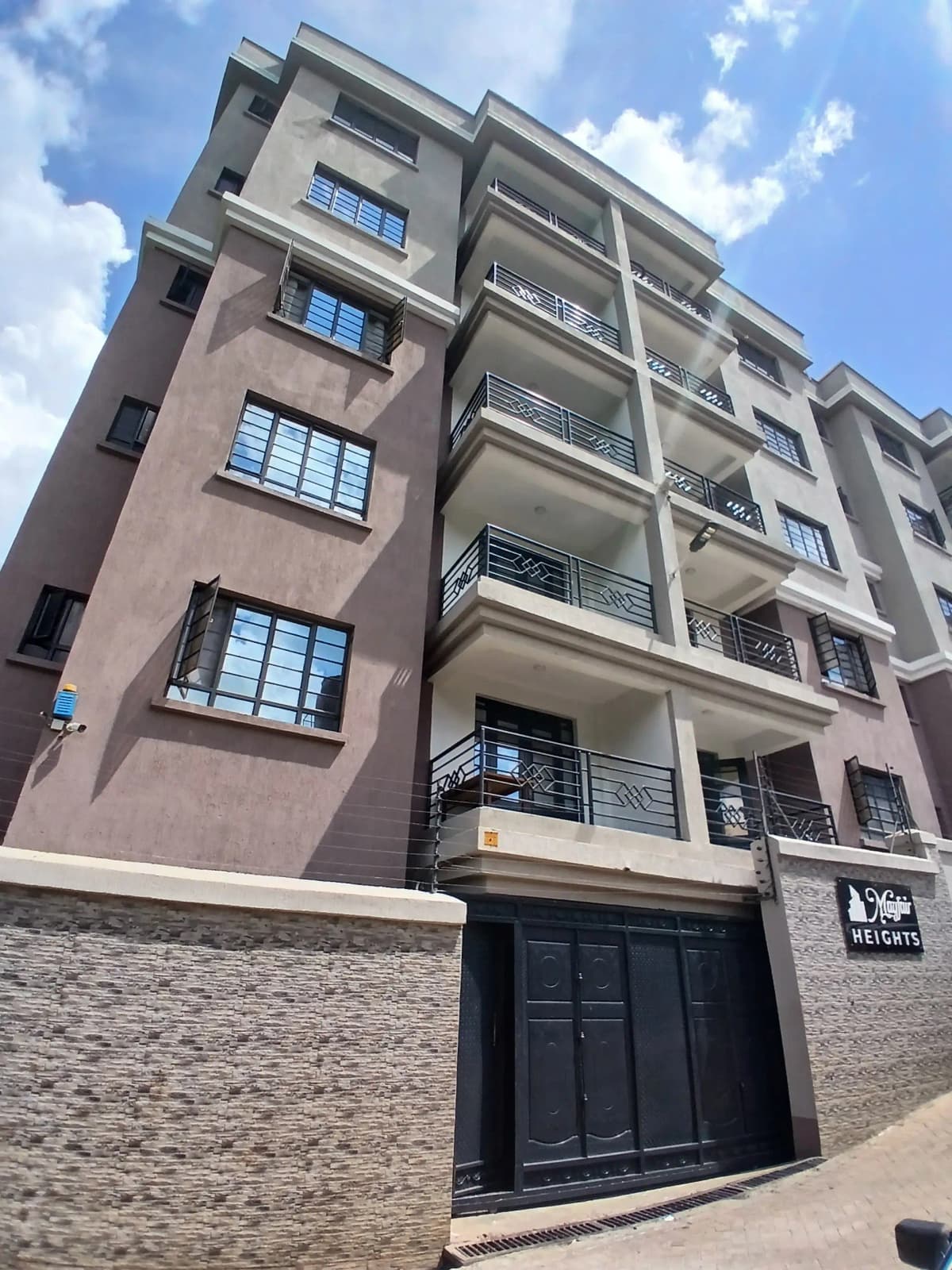 Modern multi-story residential building with balconies and gate