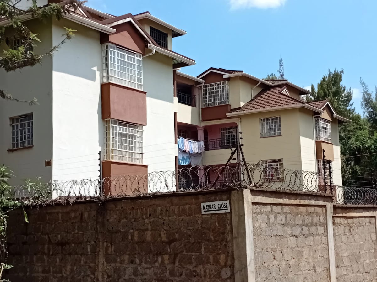 Multi-story residential building with cream and brown facade, perimeter wall