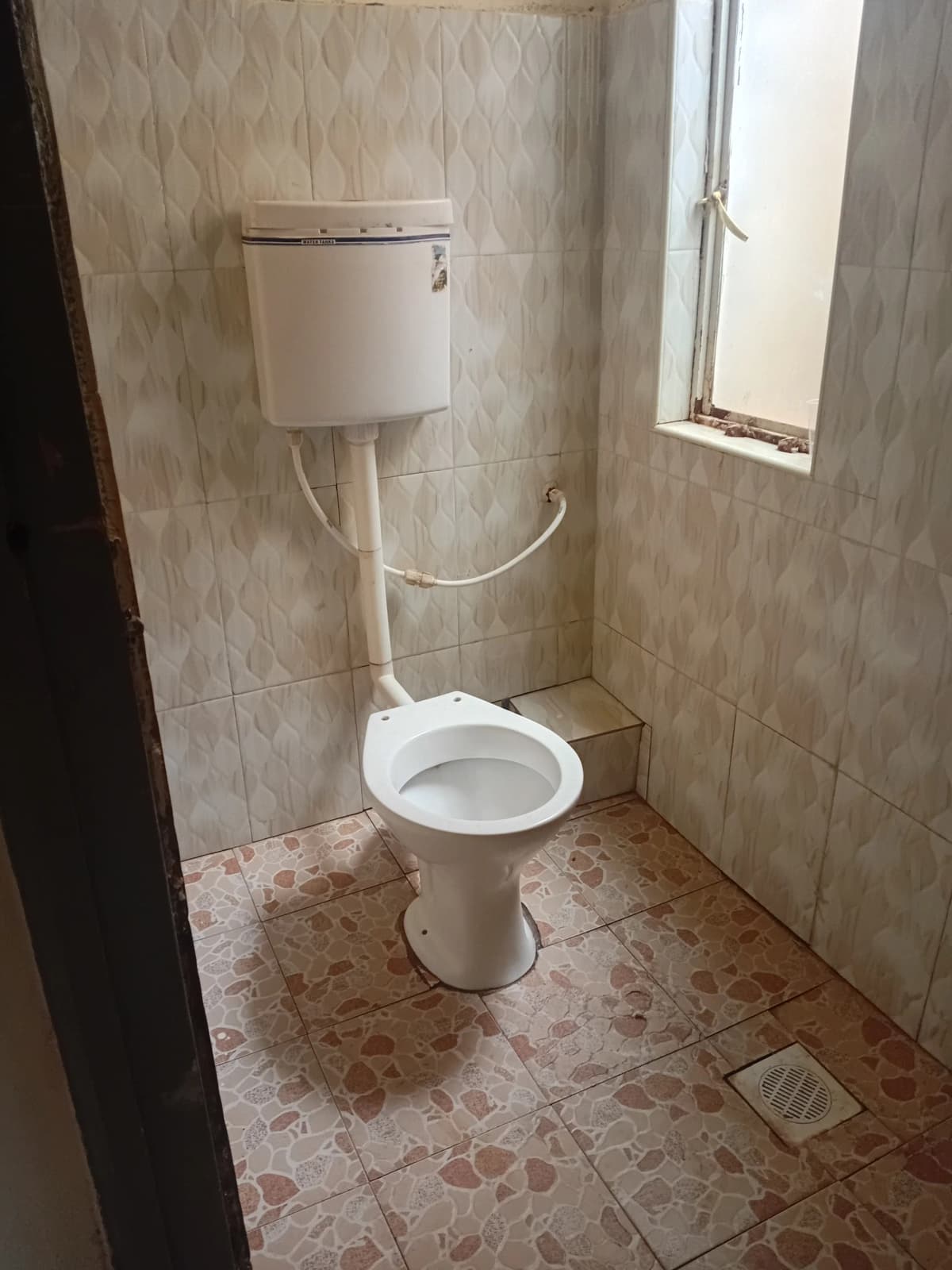 Simple toilet with overhead cistern and tiled walls