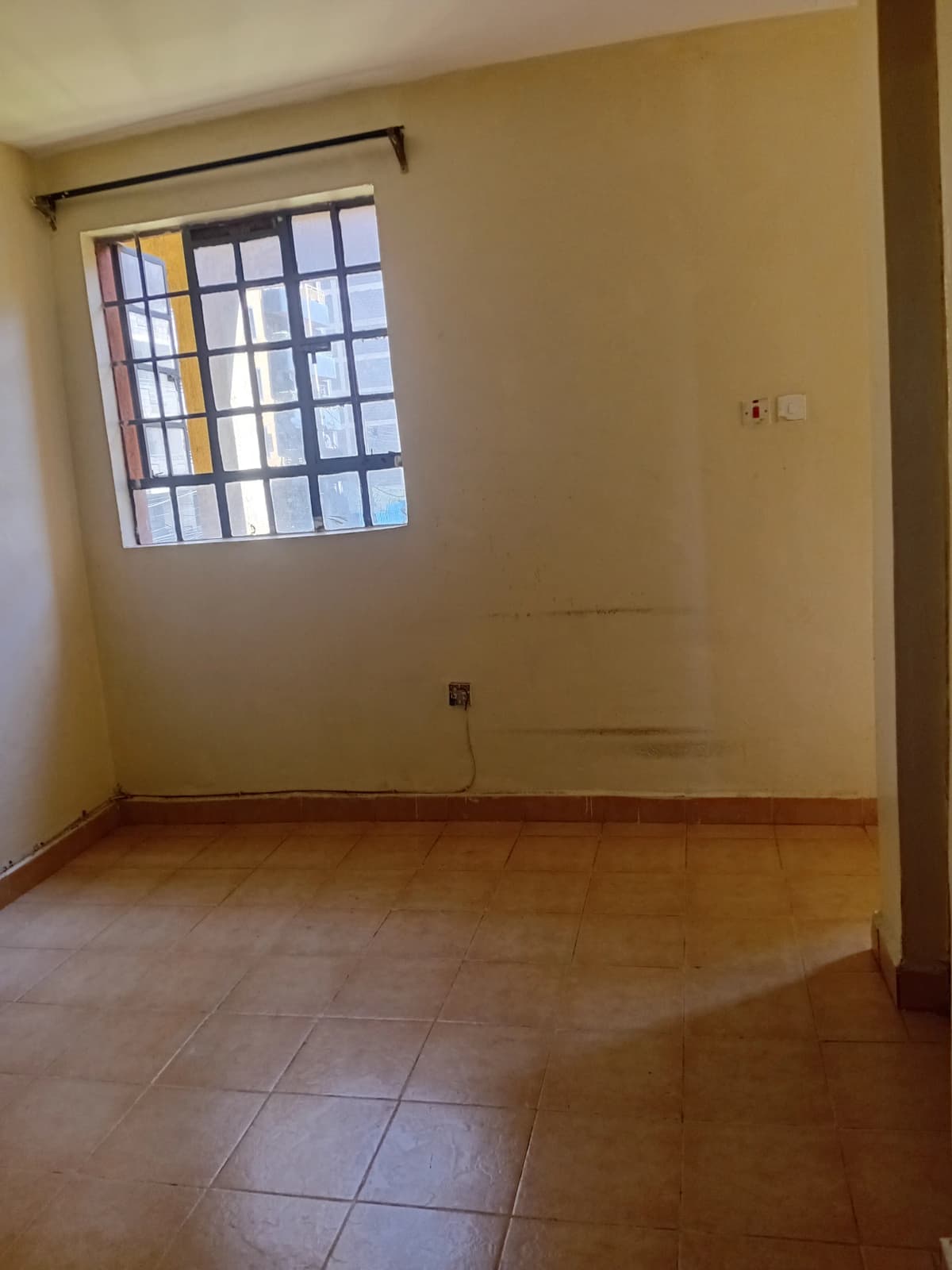 Empty bedroom with terracotta tile floor and barred window
