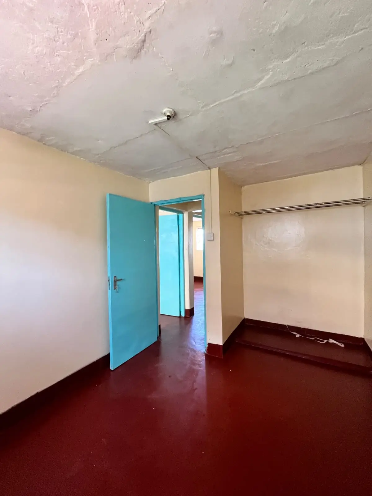 Empty bedroom with red floor and blue door, unfinished ceiling