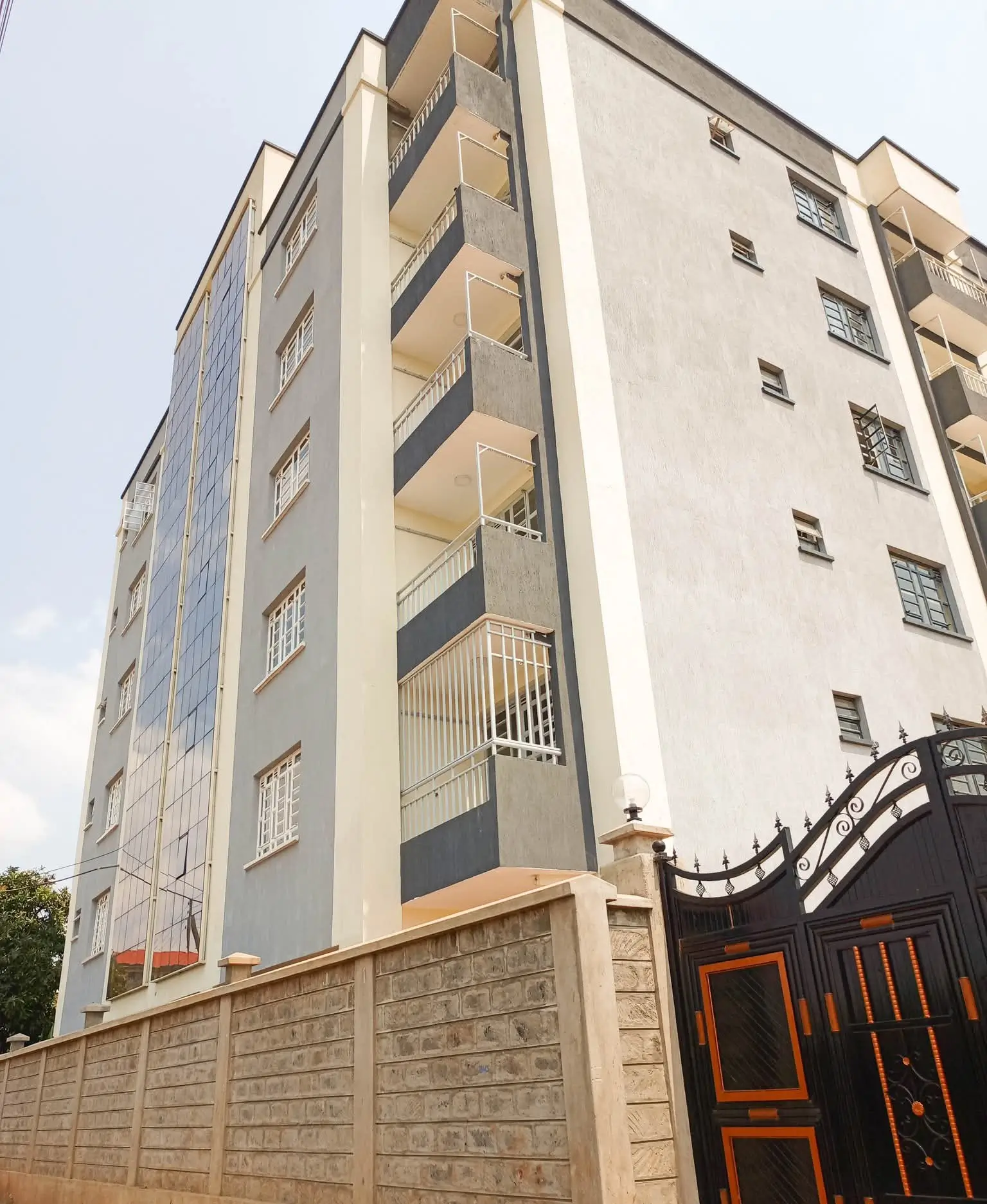 Multi-story residential building with balconies and stone perimeter wall