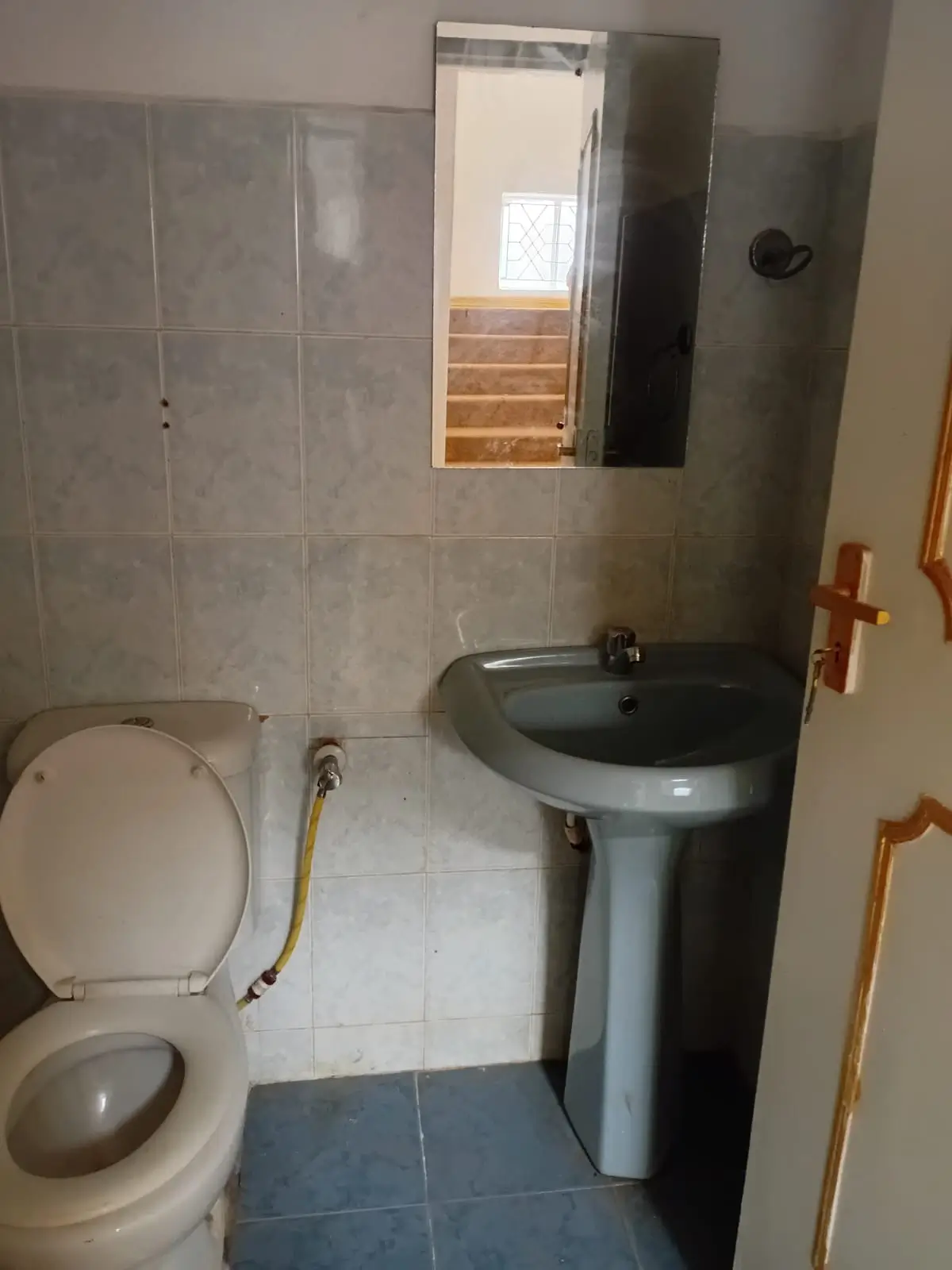 Compact bathroom with toilet, pedestal sink, tiled walls