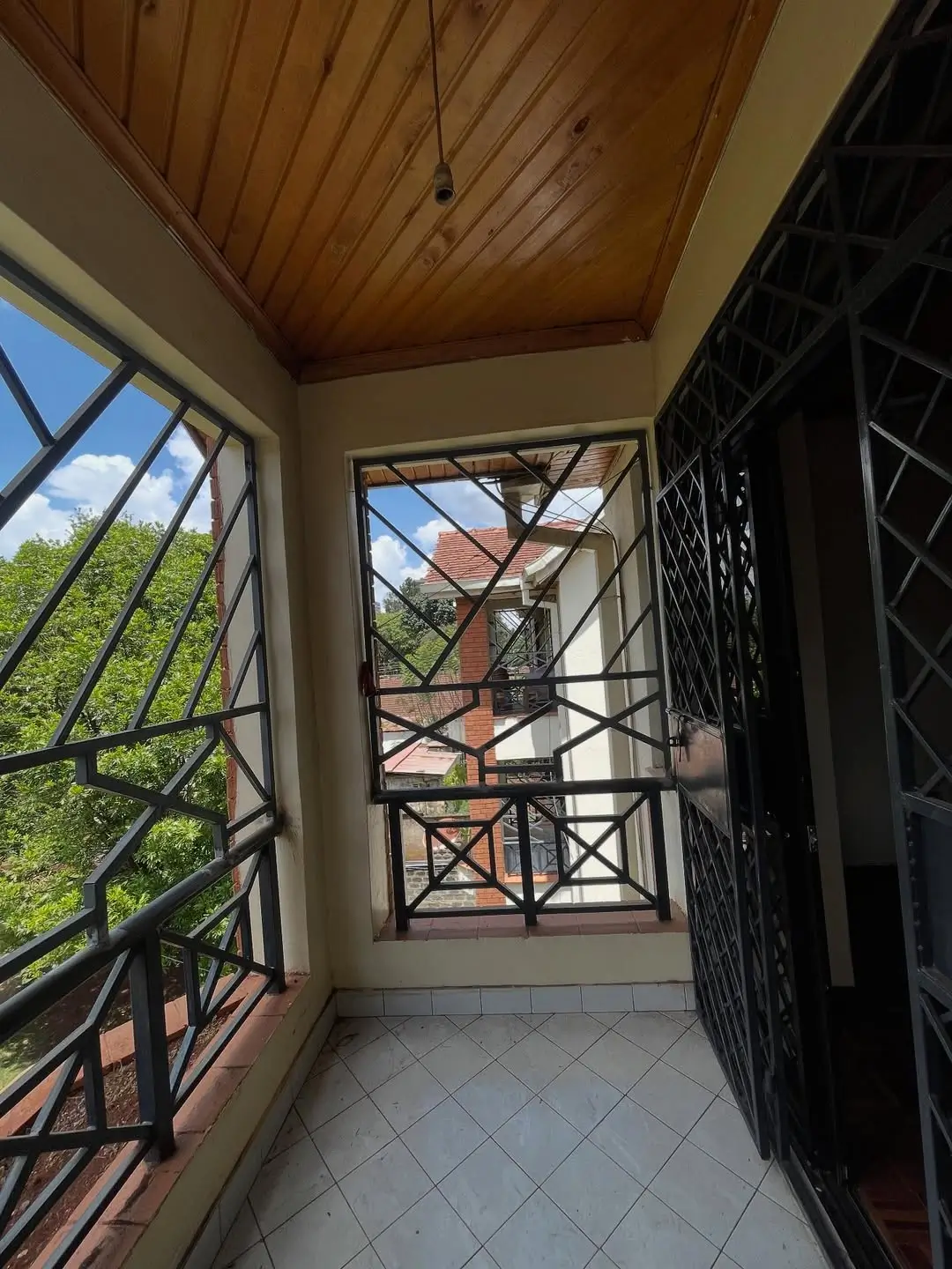 Covered balcony with wooden ceiling and security grilles overlooking compound