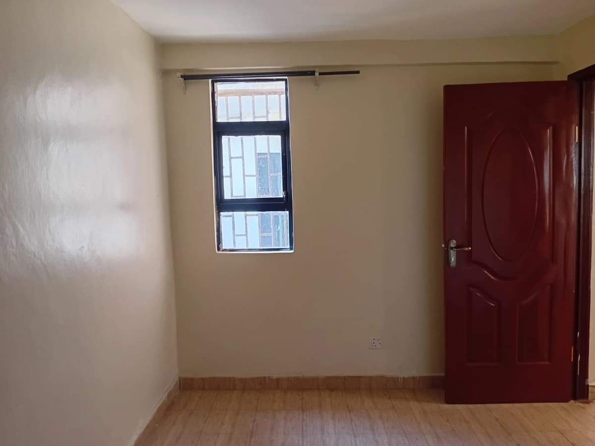 Spacious bedroom with window, wooden floor, burgundy door