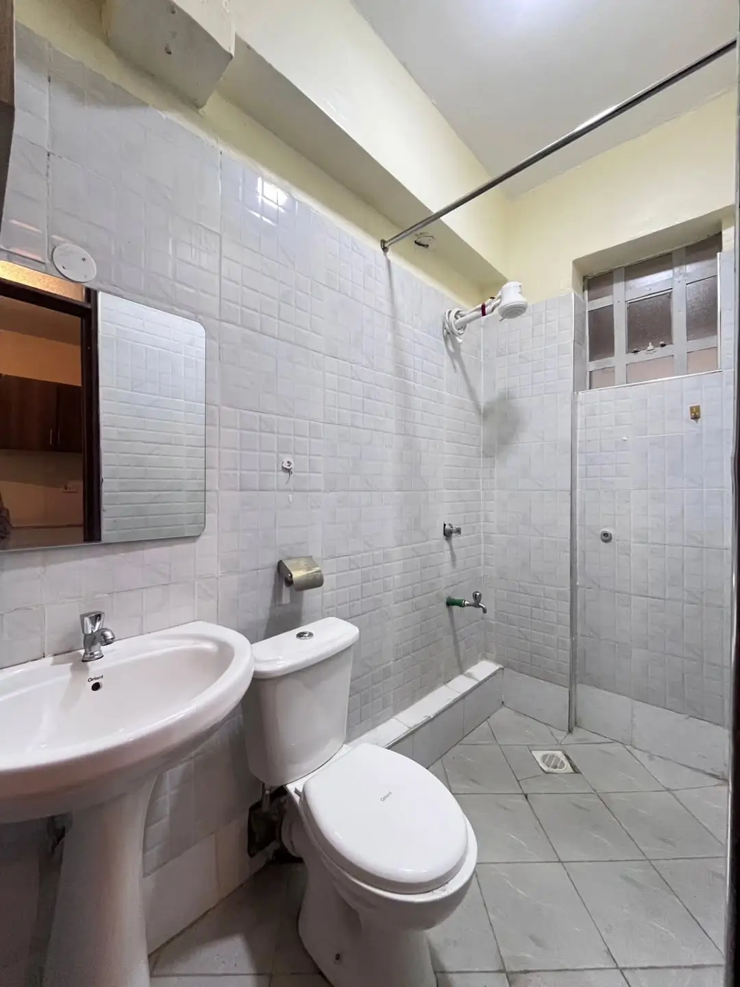 Clean bathroom with white tiles, toilet, sink, shower area.
