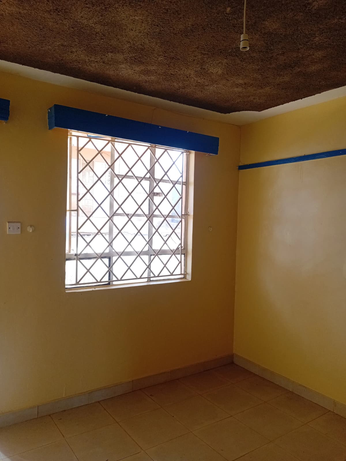 Bright yellow bedroom with barred window and tiled floor
