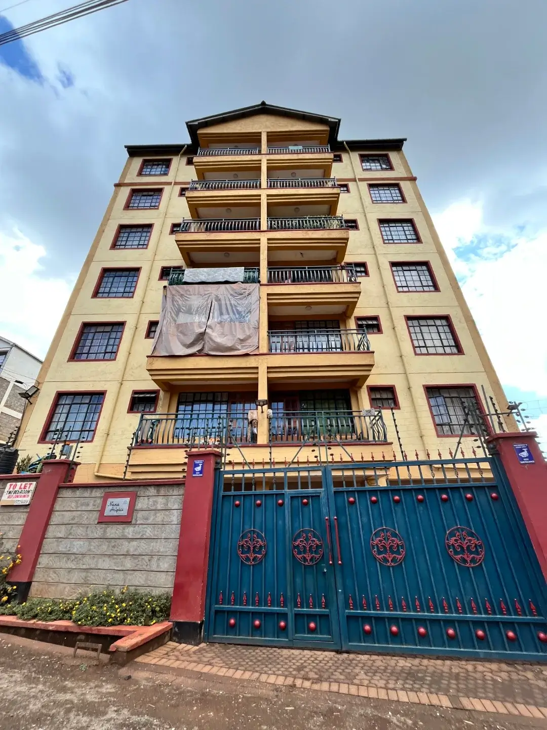 Multi-story residential building with balconies and blue gate entrance