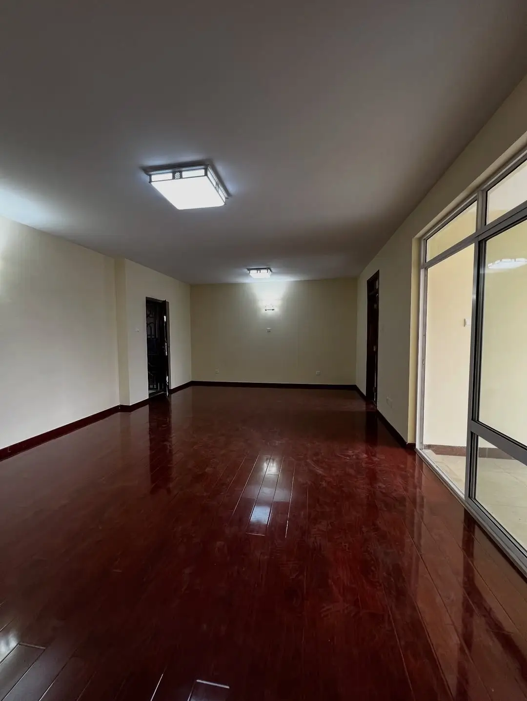Spacious empty room with burgundy polished flooring and large windows