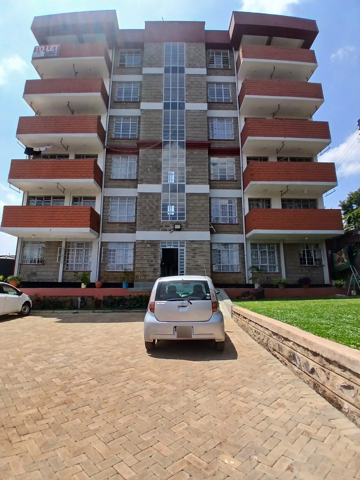 Modern multi-story apartment building with red balconies and driveway